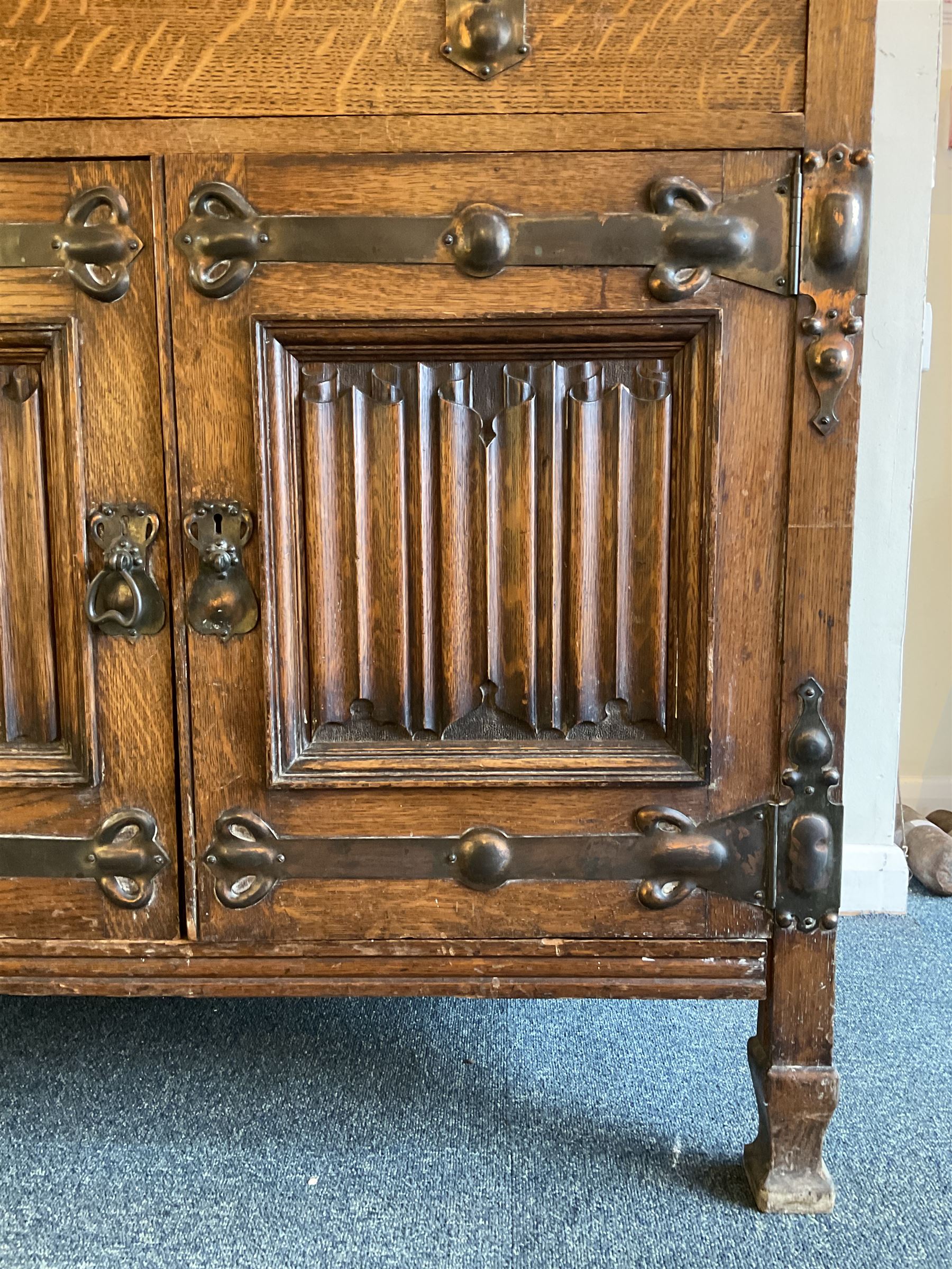 Shapland and Petter - Arts & Crafts period oak dresser, raised gallery top with spade balustrade, central bevelled mirror flanked by two cabinet, astragal glazed doors with yellow tinted glass and bullseye panes, the sides with pierced heart shaped decoration, fitted with two drawers and two double cupboards, enclosed by linenfold panelled doors,  copper work strap hinges and fixtures, on shaped spade feet, the locks stamped 'S&P'