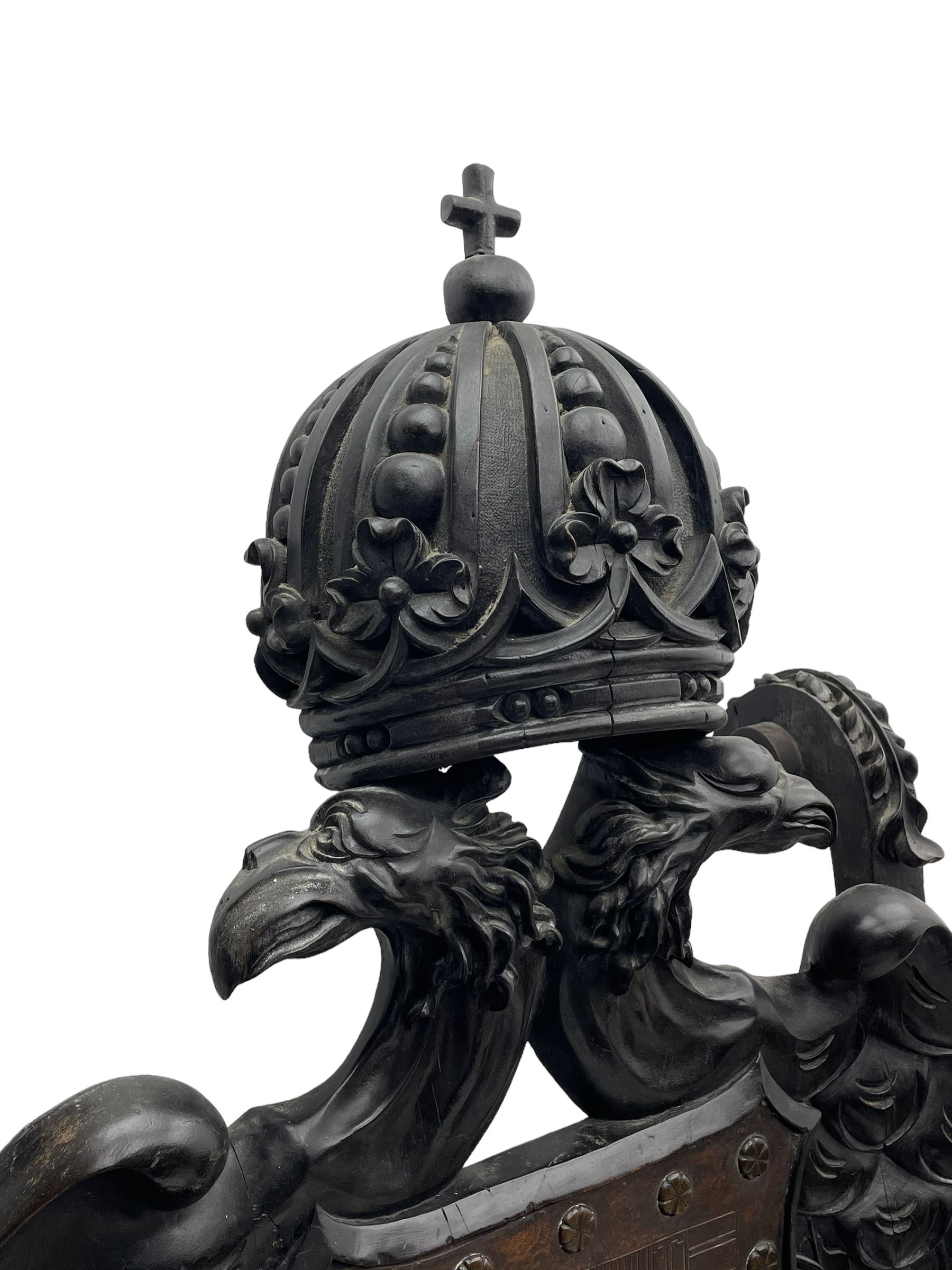 Grand mid-to-late 19th century heavily carved beech framed throne chair, the crown pediment carved with flower heads and cross finial, scroll and acanthus carved upright supports with twin perching griffin back enclosing etched leather work heraldic shield with castle and lion motifs over splayed feathers, flower head carved down sweeping arms with grotesque carved terminals, the seat rails carved with further flower heads on moulded supports with oversized ball and claw carved feet

Provenance: A very similar chair was used in the filming of Stanley Kubrick's 'Eyes Wide Shut' (1999)
