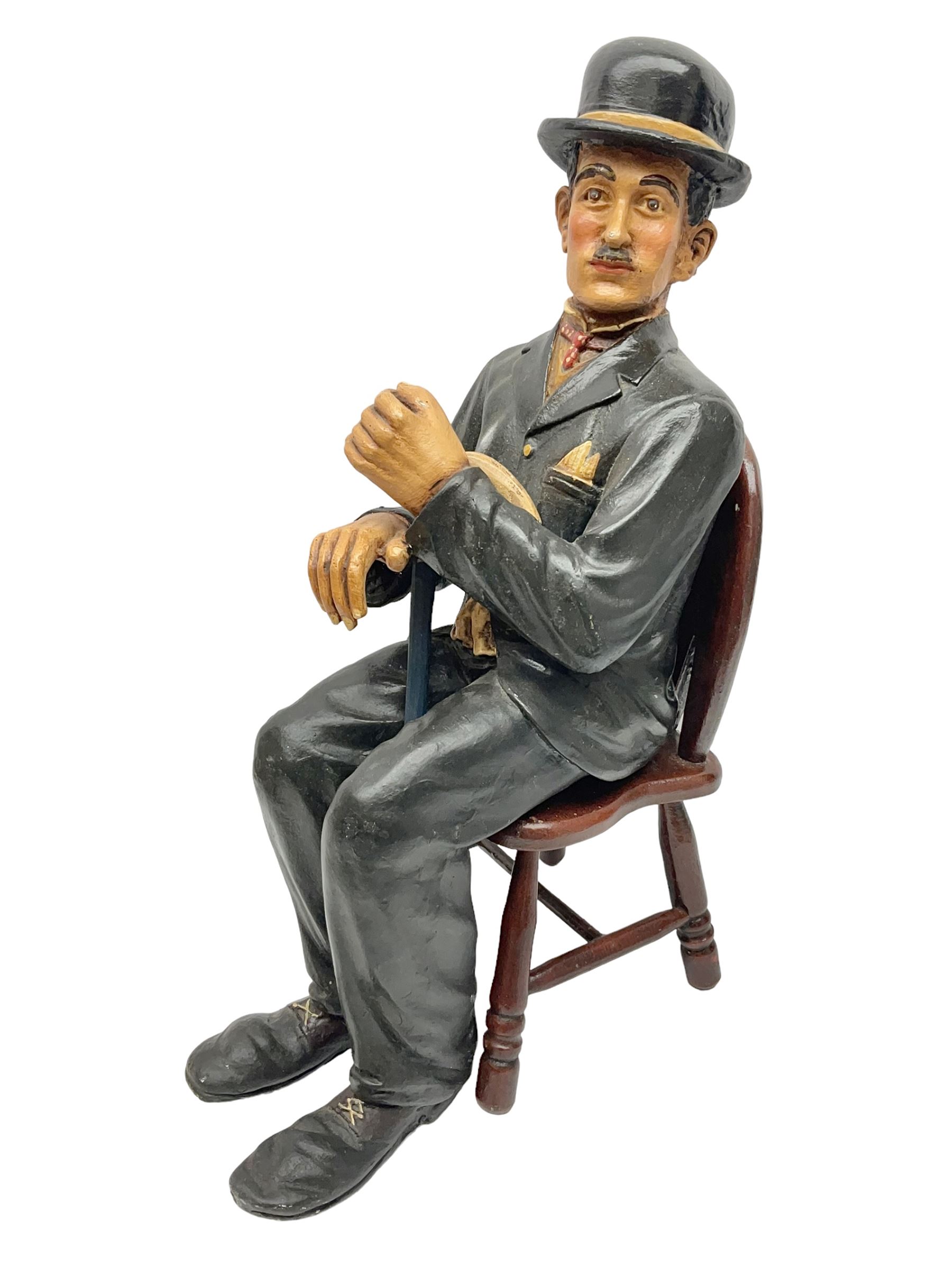 Large painted composite figure of Charlie Chaplin, seated upon wooden chair, H54cm