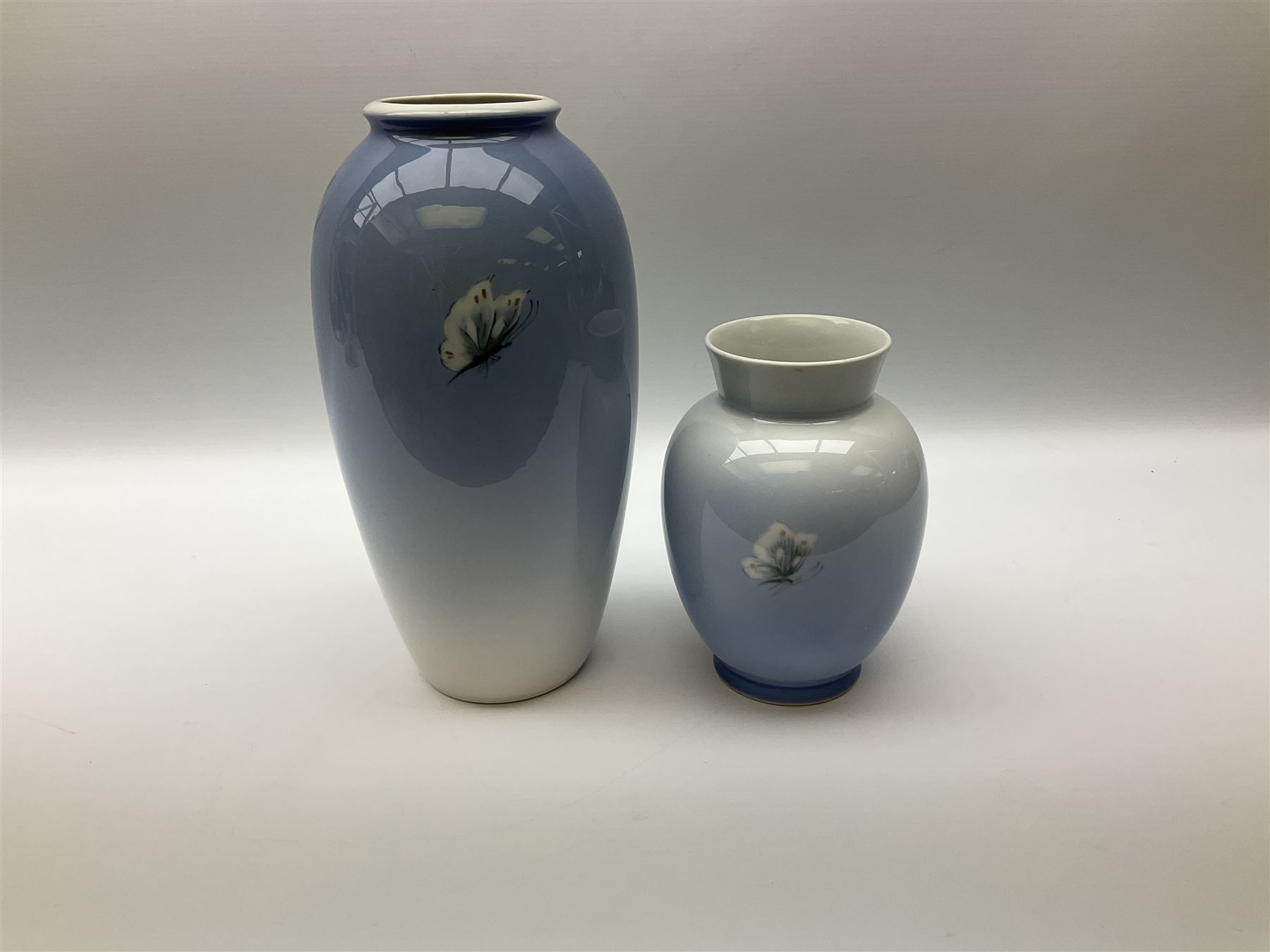 Two Royal Copenhagen vases, first example a vase of baluster form with apple blossom design on a pale blue ground, model no 2629 design no 2129 H27.5cm, second example a vase of ovoid form, with flower and butterfly decoration, model no 2667 design no 36 H17.5cm. 