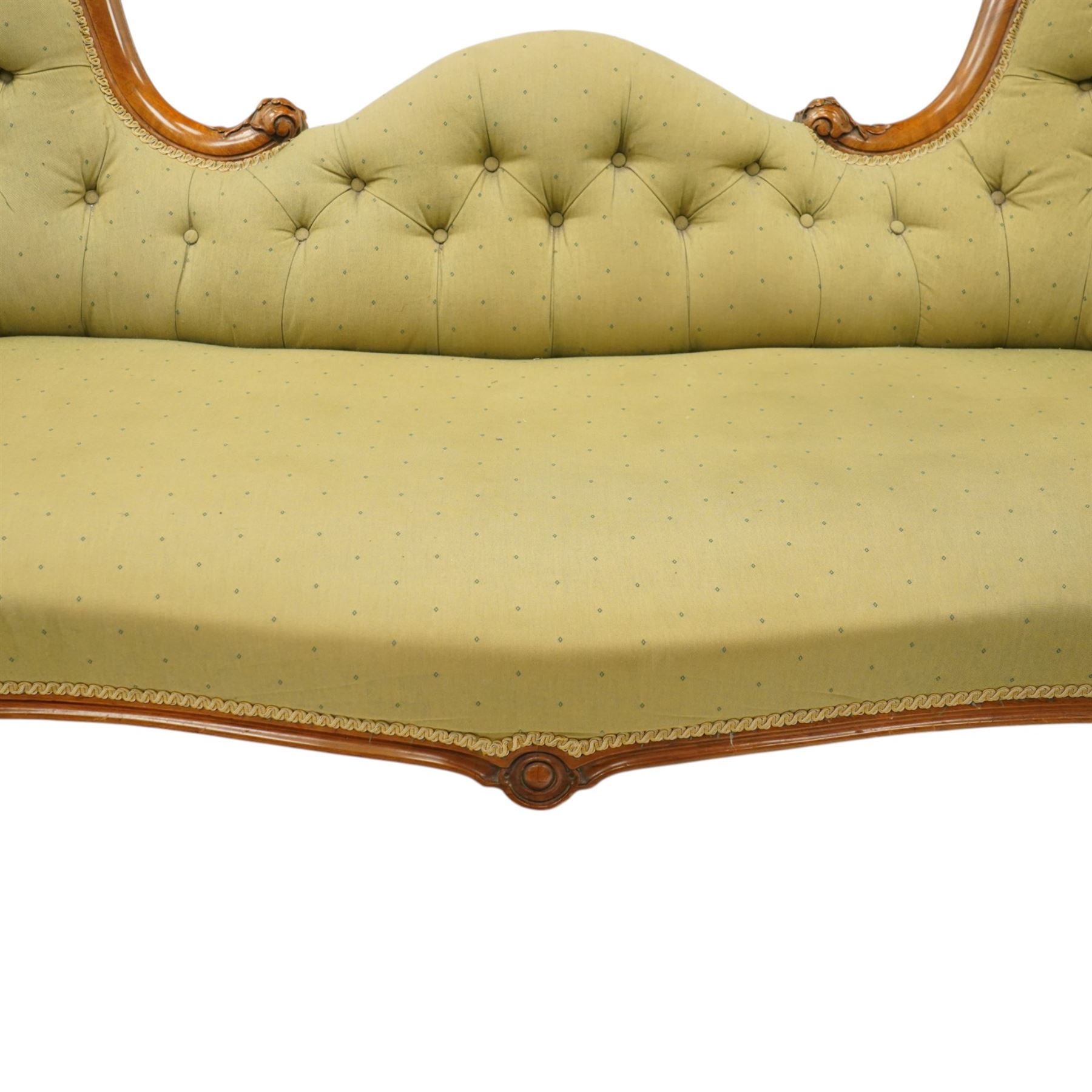 Victorian mahogany framed double ended chaise longue, serpentine button upholstered back with raised scrolled ends, padded arms and stuff-over seat upholstered in green fabric, carved showframe with foliate terminals and scroll supports, on short cabriole legs with brass castors