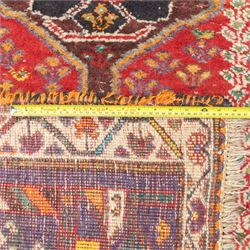 Northwestern Persian village rug, madder red field, with serrated central panel enclosing three linked lozenge medallions, polychromed spandrels, ivory border, and geometric guard stripes  