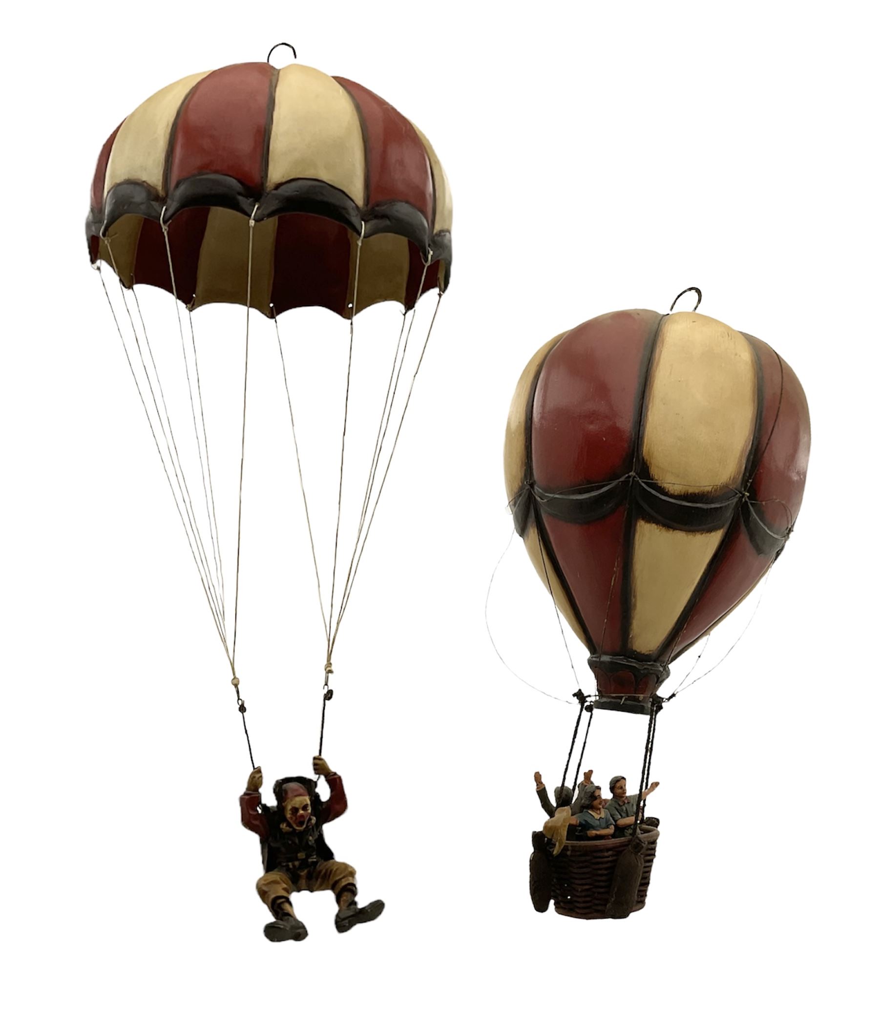 Painted wooden hanging model of a hot air balloon group, the balloon above a wicker basket complete with sandbags and figures, together with a similar example with a clown figure below, H68cm