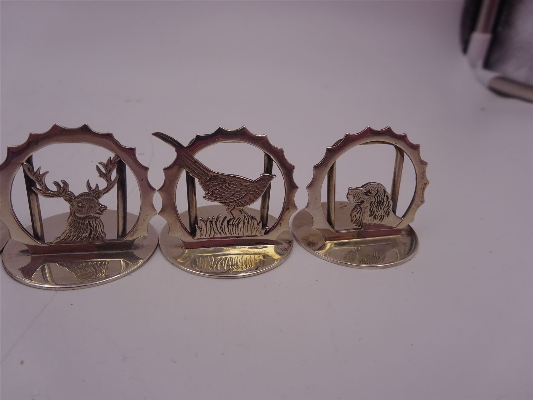 Set of six modern silver place card holders, each of circular form with pierced depictions of a partridge, spaniel, pheasant, stag, woodcock and duck, hallmarked J A Campbell, London 1985, contained within a velvet and silk lined fitted case, H3cm