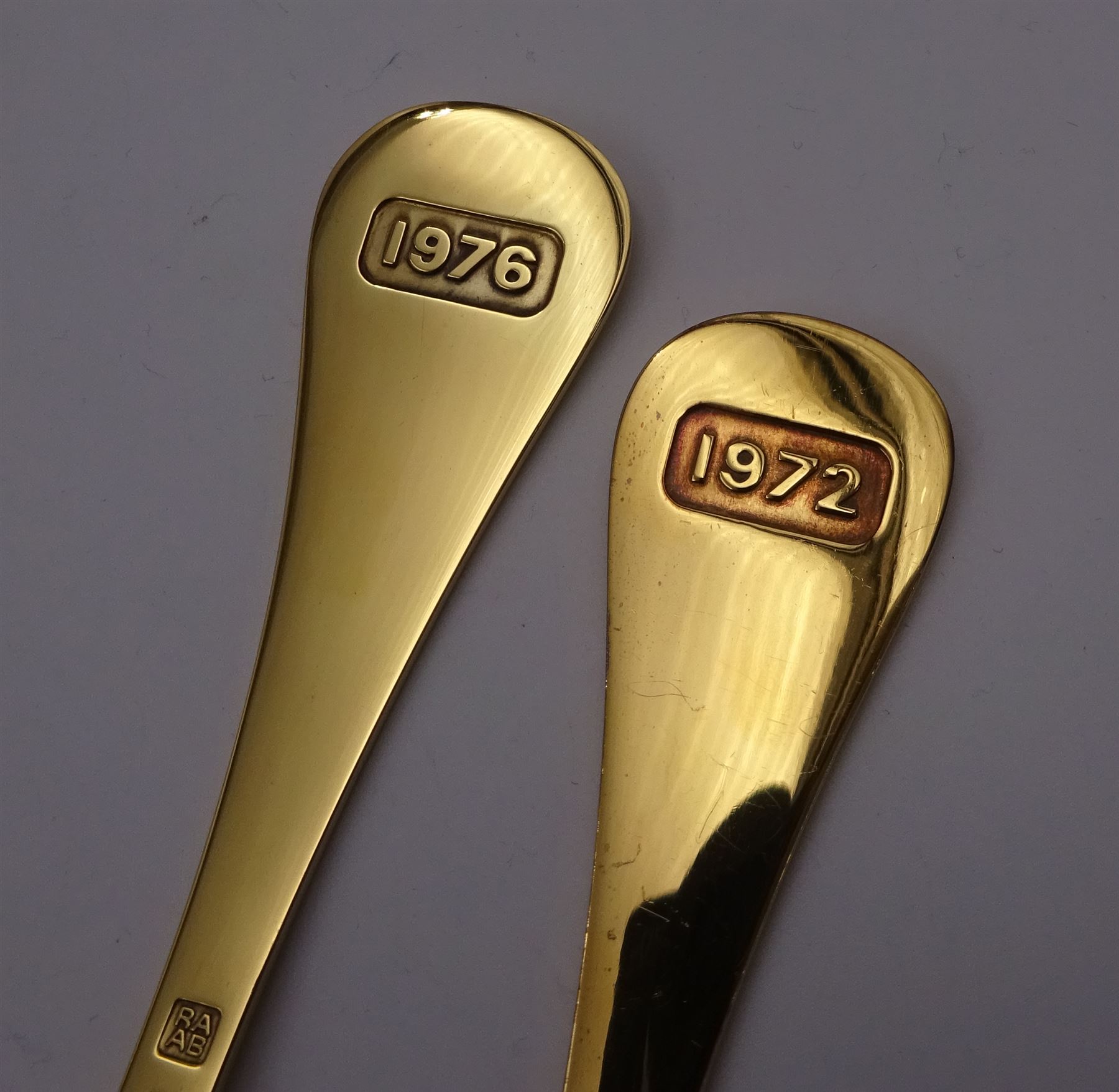 Two Danish silver-gilt year spoons by Georg Jensen, the first example decorated with enamel blue cornflower motif, dated 1972, in original pouch, the second example decorated with enamel pink briar rose motif, dated 1976, in original box, each impressed on underside RA AB, Sterling Denmark, and marked for Georg Jensen, together with two further examples by A.Michelson, the first with orange enamel fan design, dated 1965, impressed on underside A.Michelsen Sterling Danmark, TH, the second with enamel family scene, dated 1973, impressed on underside 925 S A.Michelsen Sterling Danmark, B Spang Olsen, approximate gross weight 6.11ozt (190.4 grams)