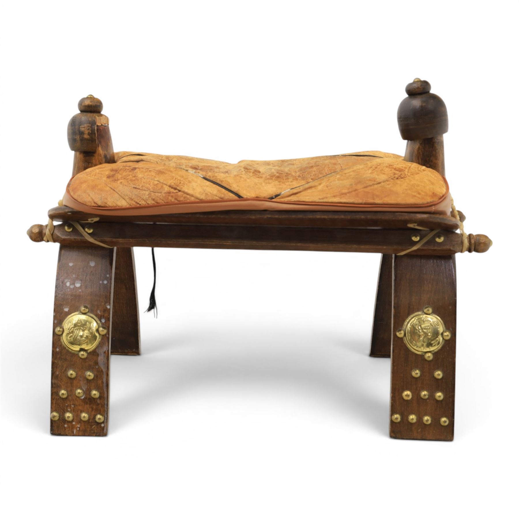 20th century Camel stool, with wooden turned finials, above a tooled leather seat, curved supports with brass applications 