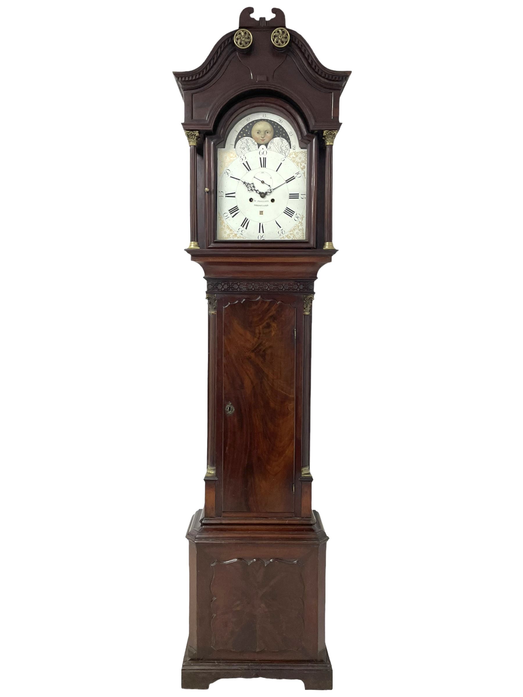 W. Phillips of Bromyard - 8-day mahogany longcase with a painted moon roller dial, c 1790,
swans neck pediment with dog tooth moulding, raised carving and  brass paterie, break arch hood door beneath flanked by reeded pilasters with brass Corinthian capitals, trunk with a blind fret, reeded quarter columns and long wavy topped door,
Plinth with a deep moulding and canted corners raised on a shaped base, painted dial with gesso spandrels, Roman numerals, five minute Arabic's and minute dots, with steel hands, seconds dial and square date aperture, dial pinned to a rack striking movement with an anchor escapement, striking the hours on a cast bell. A clockmaker by the name of John Phillips is recorded as working in Bromyard (Worcs)  in the early to mid 18th century, certainly by 1770-90. W. Phillips was possibly an unrecorded son or brother also working in the same family clockmaking business during the later part of the 18th century.
