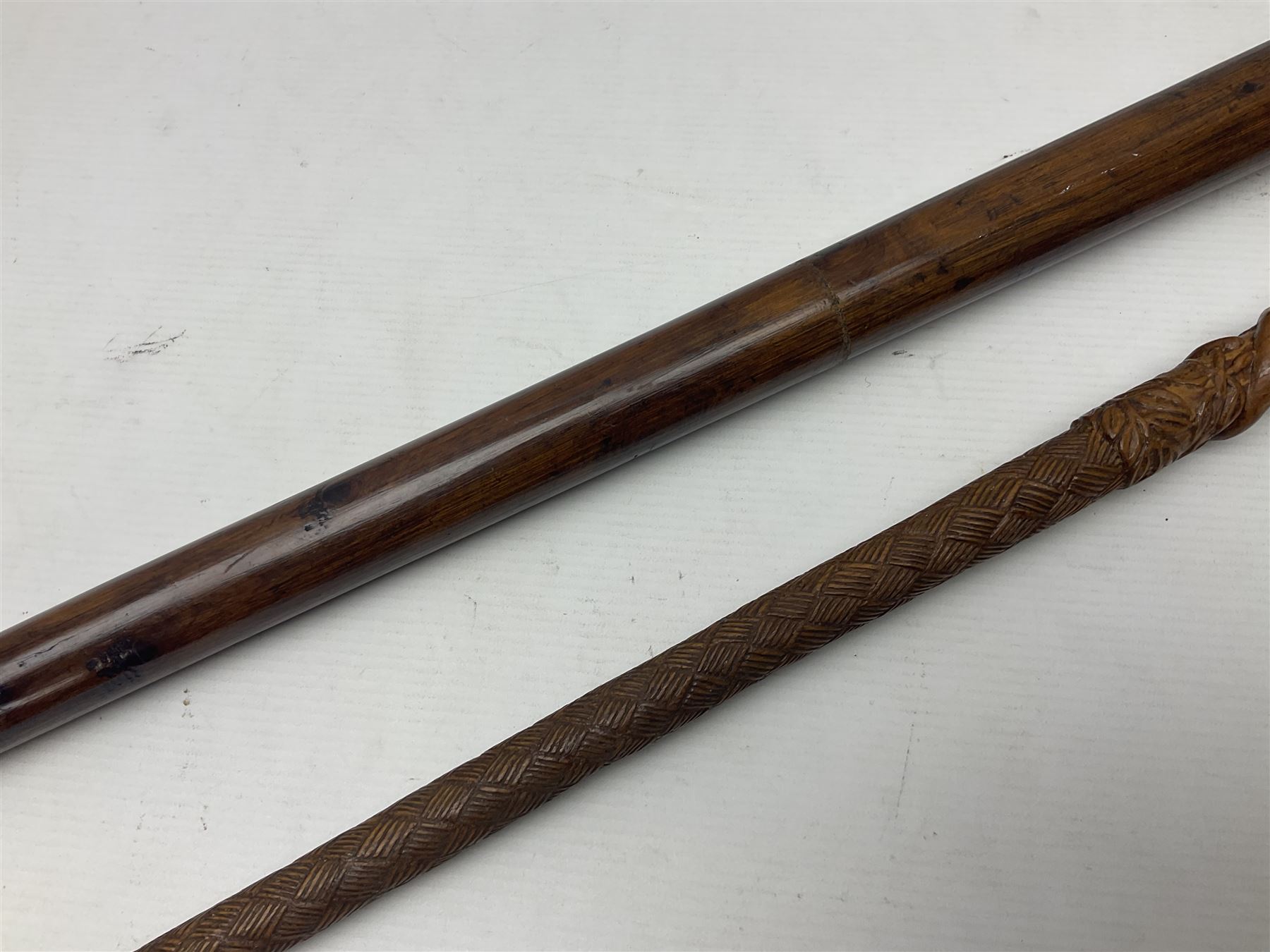19th century wooden walking stick, the handle carved as a snake within a clenched fist, the cane carved with foliate and cross hatched decoration, with a metal spike to base, together with a turned wooden walking stick, with lacquered rope nautical knot handle, tallest L96.5cm