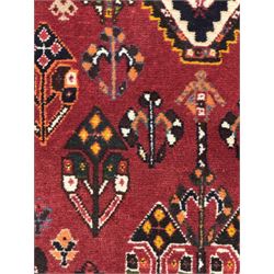 Persian Qashqai crimson ground runner, the field decorated with repeating diamond-shaped medallions flanked by angular floral motifs, the spandrels with intricate boteh designs, framed by an ivory border with stylised floral patterns and scrolling vines