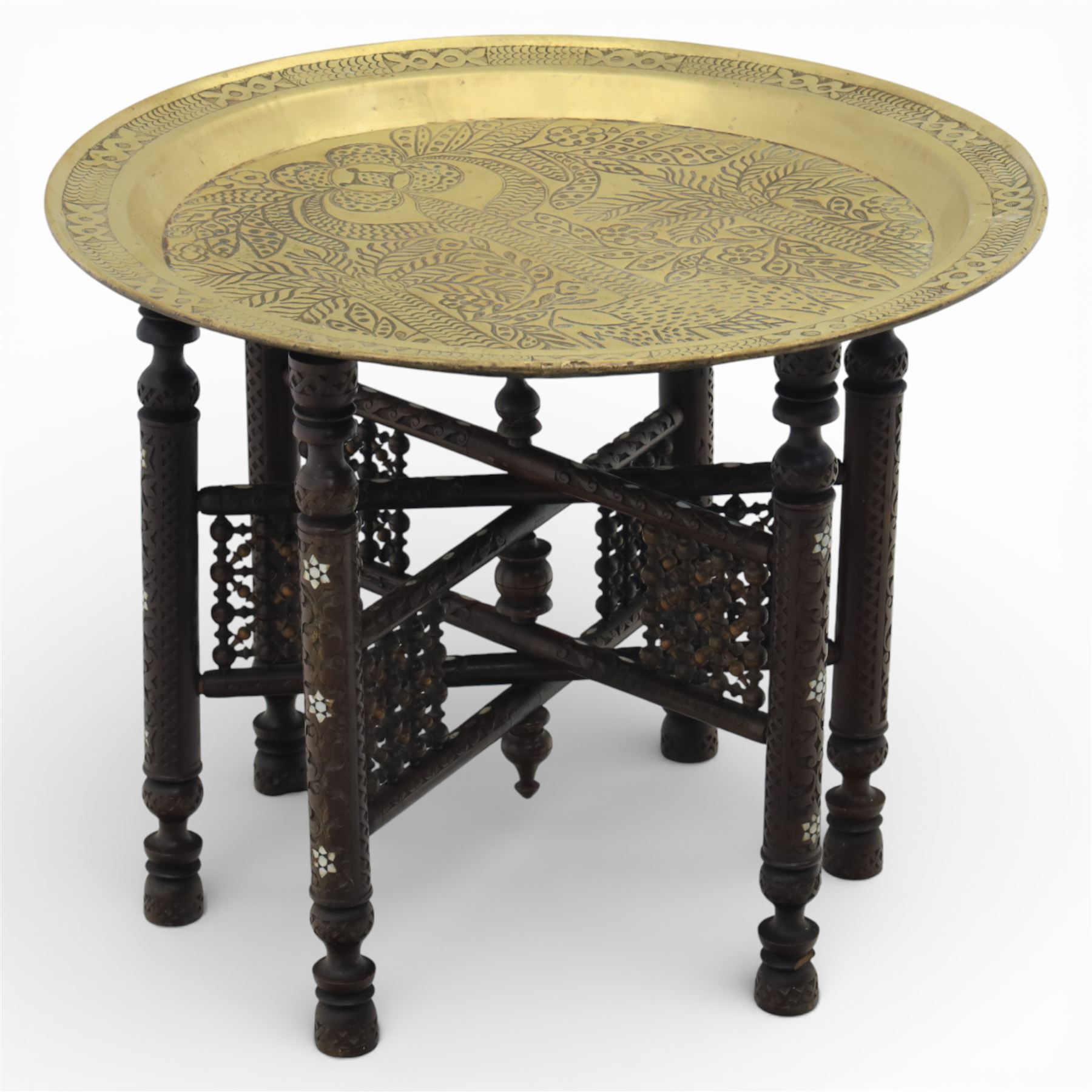 20th century Eastern brass charger topped table, the circular brass trap chased with an elephant, palm tress and flowering vines, supported upon a folding stand with six turned legs with inlaid detail, united by turned supports