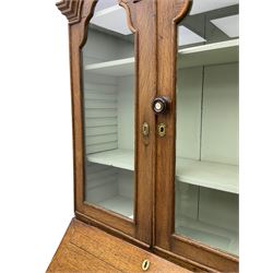 George III oak bookcase on bureau, the double arched top enclosed by two shaped glazed doors, fall-front concealing fitted interior, over four graduating cock-beaded drawers, on bracket feet