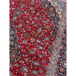 Persian Kashan crimson ground carpet, floral pattern indigo ground central medallion and matching spandrels, the field decorated densely with scrolling foliate patterns and floral motifs, the main border decorated with scrolling branches and palmettes, within floral pattern guard stripes