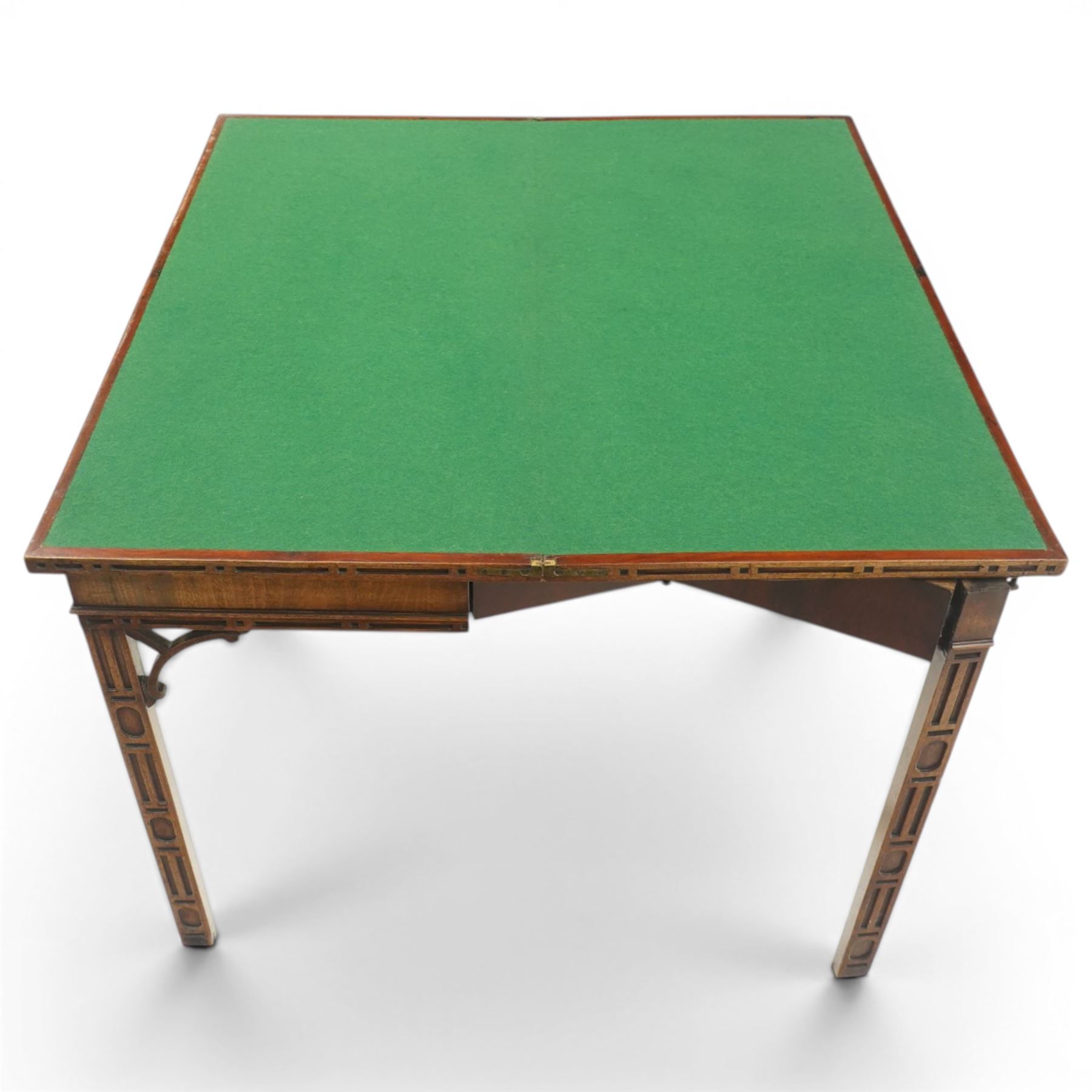 George III Chippendale design mahogany table, the rectangular hinged top with geometric carved edge, opening to reveal a baize-lined interior supported by twin concertina rear gateleg supports, over a banded frieze and pierced C-scroll spandrels, the inner chamfered square supports carved with geometric blind-fretwork detail