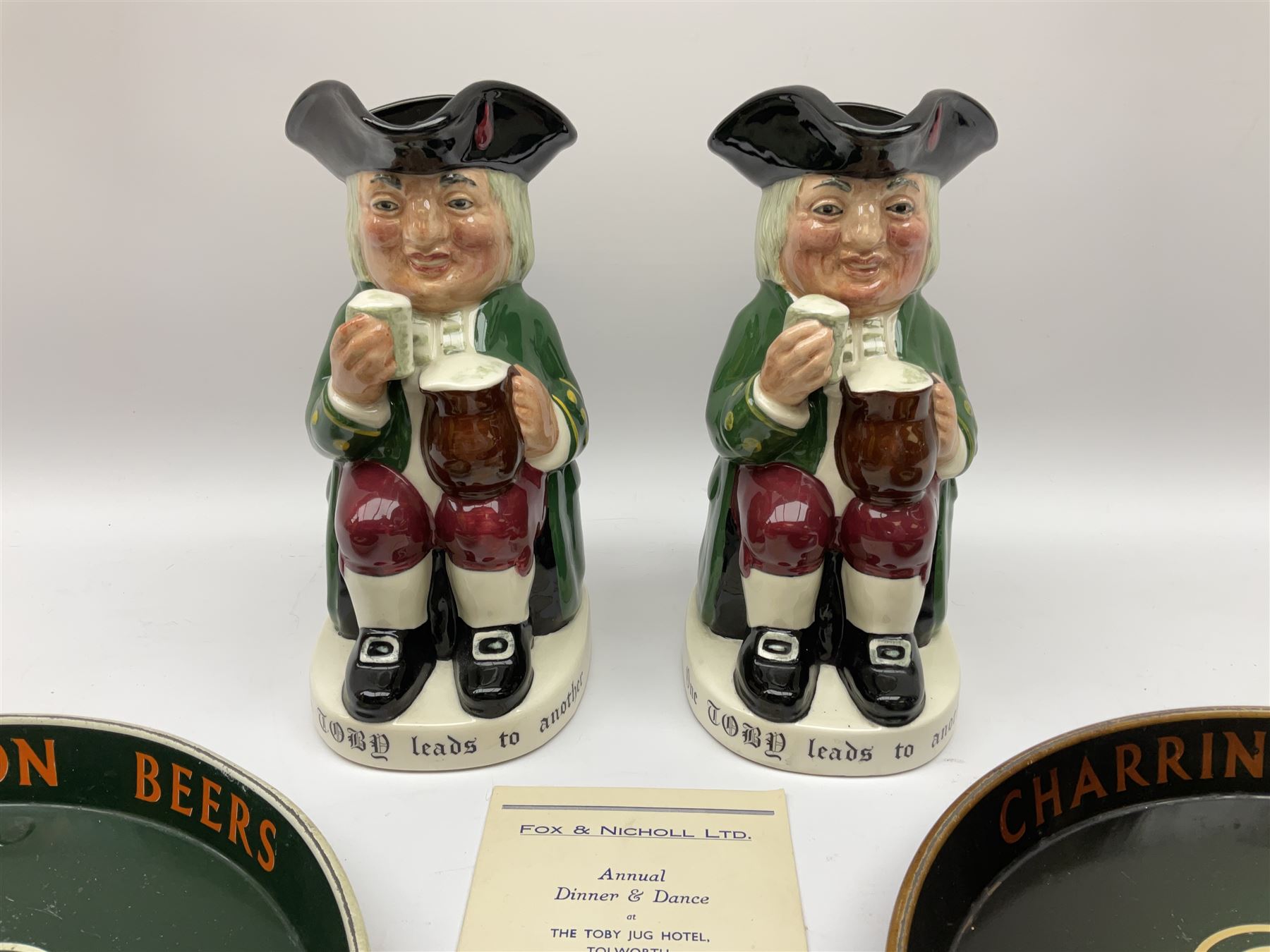 Pair of Royal Doulton Toby Ale Jugs, produced in 1934 for Charrington Ales, together with two circular metal serving trays advertising Charrington brewery, a Charrington badge awarded for 25 years of service and a 1949 menu Fox & Nicholl Ltd annual dinner dance at the toby jug hotel.  