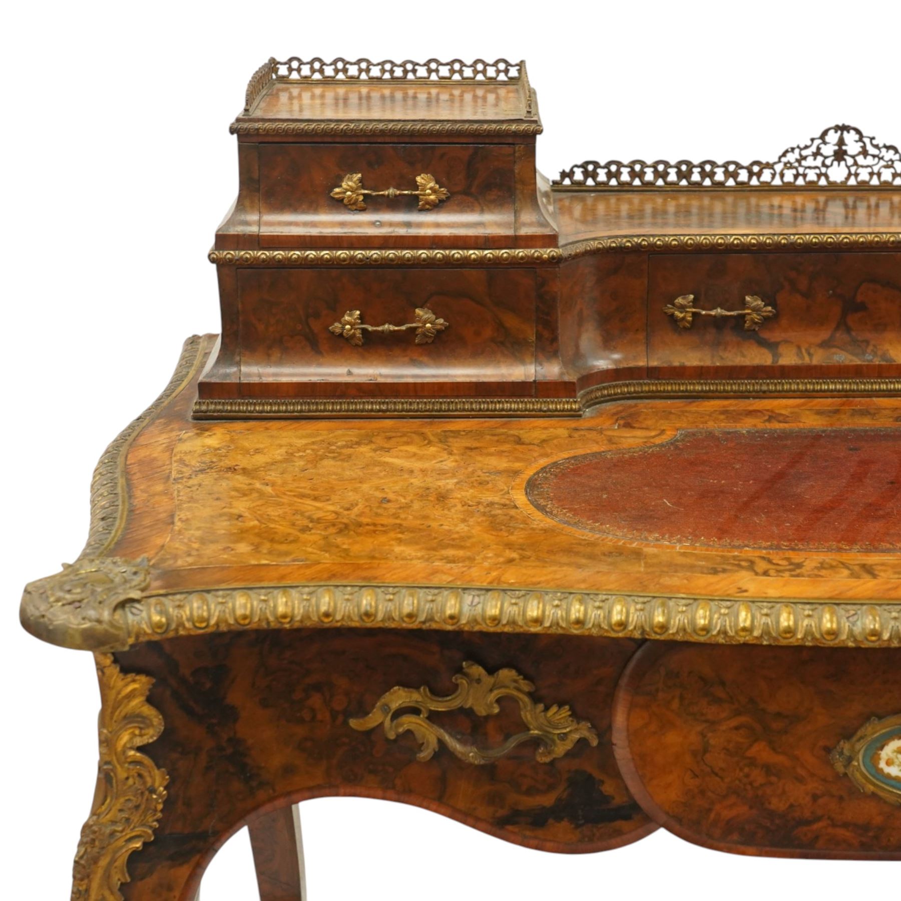 Victorian figured walnut and kingwood-banded ladies writing table, the raised superstructure with three-quarter pierced brass raised gallery back, fitted with five assorted drawers, the serpentine shaped top with oval inset leather surface, the bronze edge of egg and dart form with cartouche corners, fitted with central frieze drawer with inset Sevres-style floral ceramic plaque, raised on cabriole supports with gilt metal mounts