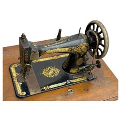 Singer - early 20th century cast iron treadle sewing machine, with hand crank wheel and oak work surface, the machine decorated with gilt foliate detail, complete with rectangular wooden cover and folding extension leaf