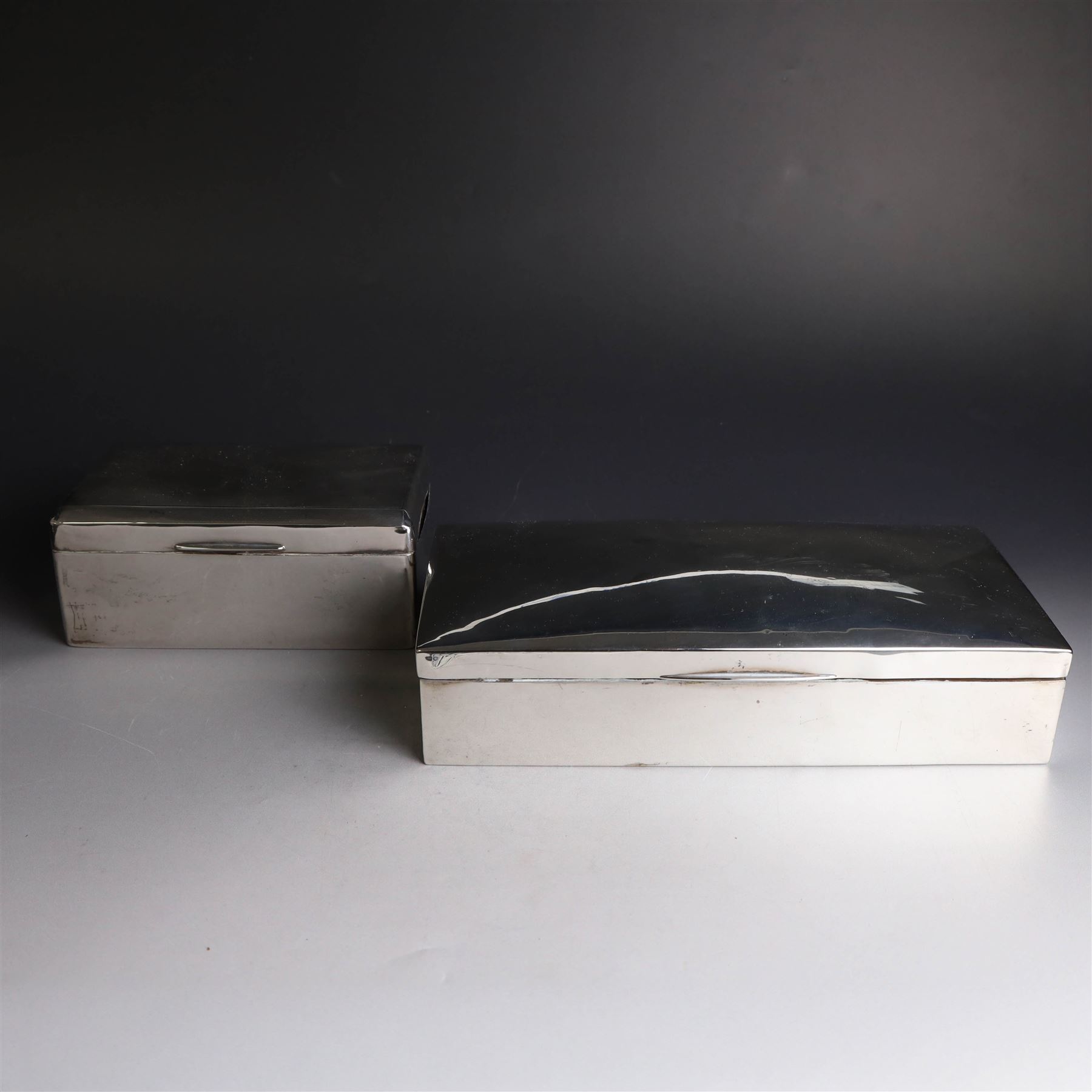 Two silver cigarette boxes, comprising early 20th century plain rectangular example with compartmentalised softwood interior, hallmarked Birmingham 1914, maker's mark indistinct, and an early 20th century example with engine turned decoration and engraved initials to cover, hallmarks worn and indistinct, largest H4.5cm, W21cm