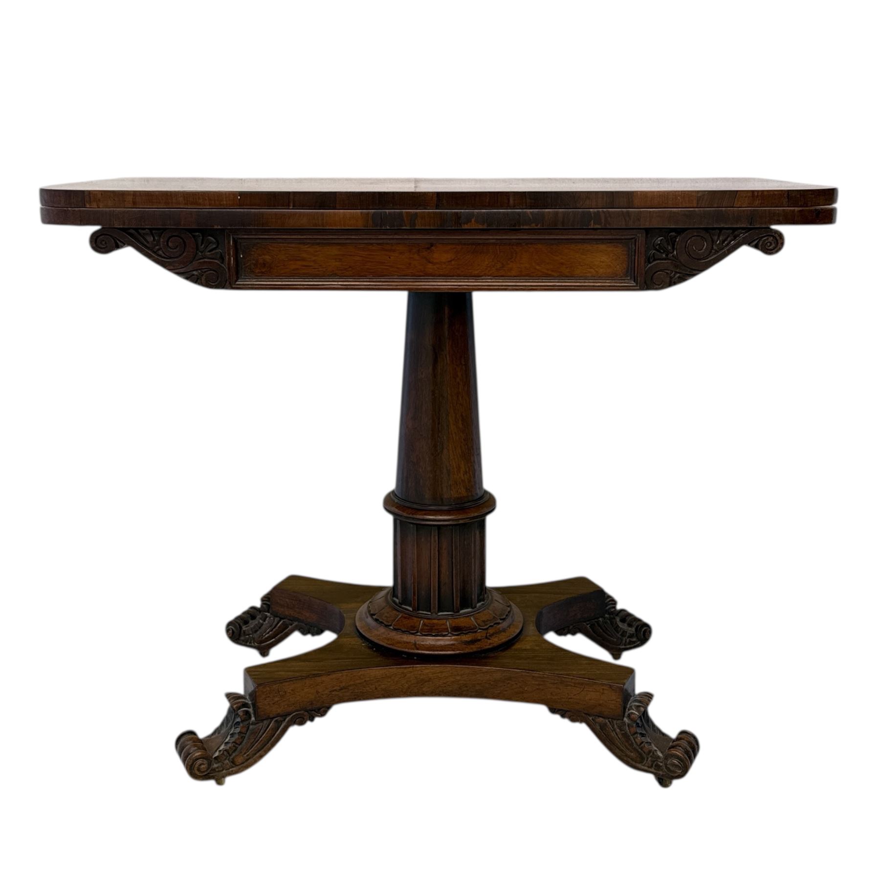 William IV rosewood card table, rounded rectangular swivel and fold-over top with plain frieze, with carved scrolled brackets above stop-fluted column with moulded collar on quadriform base with scrolled feet 