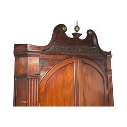 George III mahogany corner cabinet, the scrolled pediment surmounted by a brass finial and carved fretwork frieze, with fluted uprights flanking arched double doors over a painted interior fitted with shaped shelves, above a lower cupboard with twin panelled doors, on plinth base