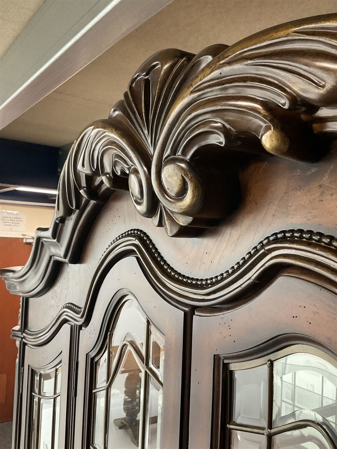 Kevin Charles American walnut display cabinet, illuminated interior, shell carved pediment above four bevel edge doors enclosing six glazed shelves above one central long drawer flanked by two short drawers, above three cupboards, carved bracket supports 