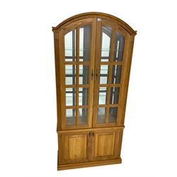 Light oak arched top display cabinet, mirrored interior enclosed by two glazed doors, double panelled cupboard below, on plinth base