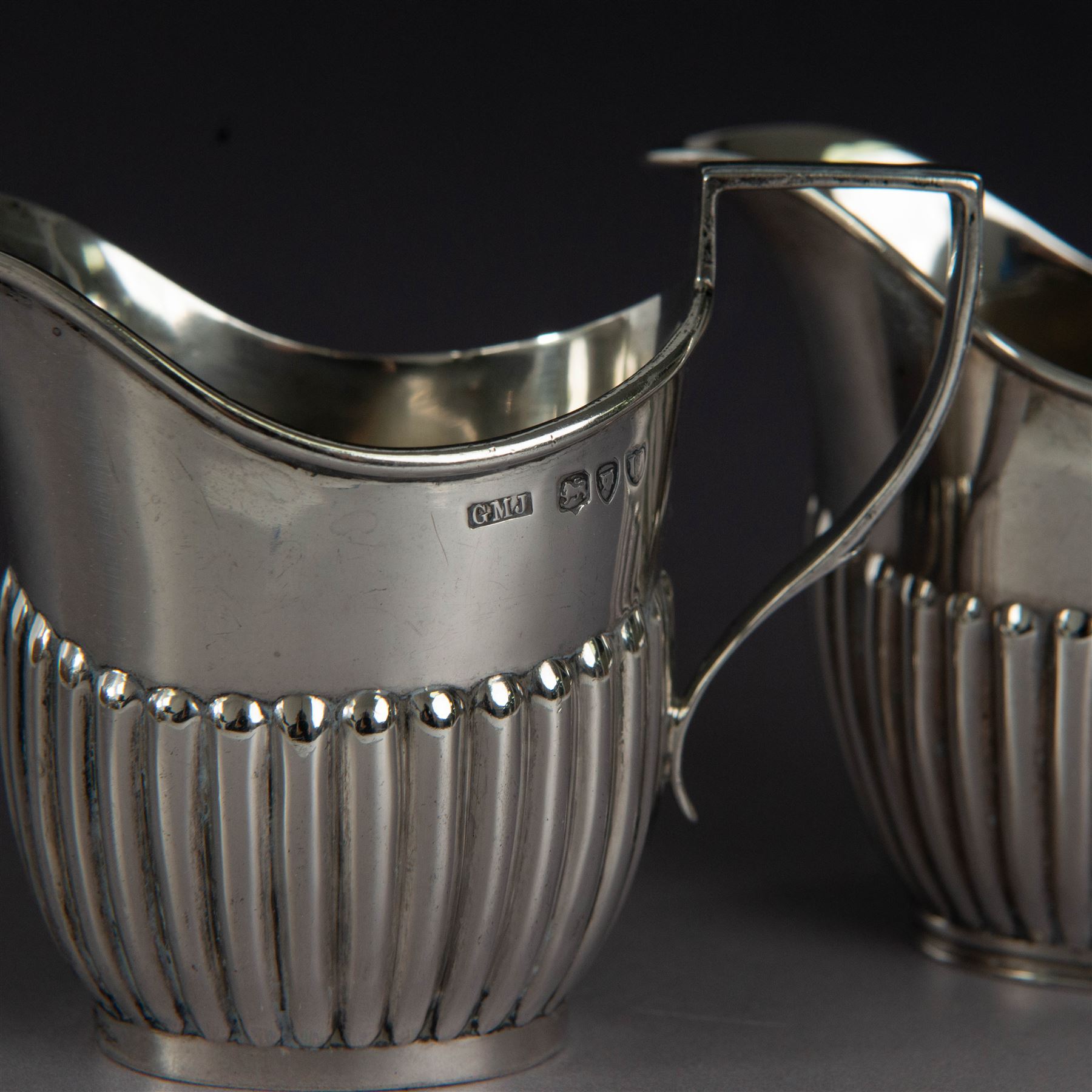 Victorian silver two piece bachelors tea service, comprising teapot and milk jug, of oval part fluted form, the teapot with ebonised wooden handle and finial, hallmarked Josiah Williams & Co, London 1895, together with a silver milk jug and open sucrier, of similar form, hallmarked William Hutton & Sons, London 1898