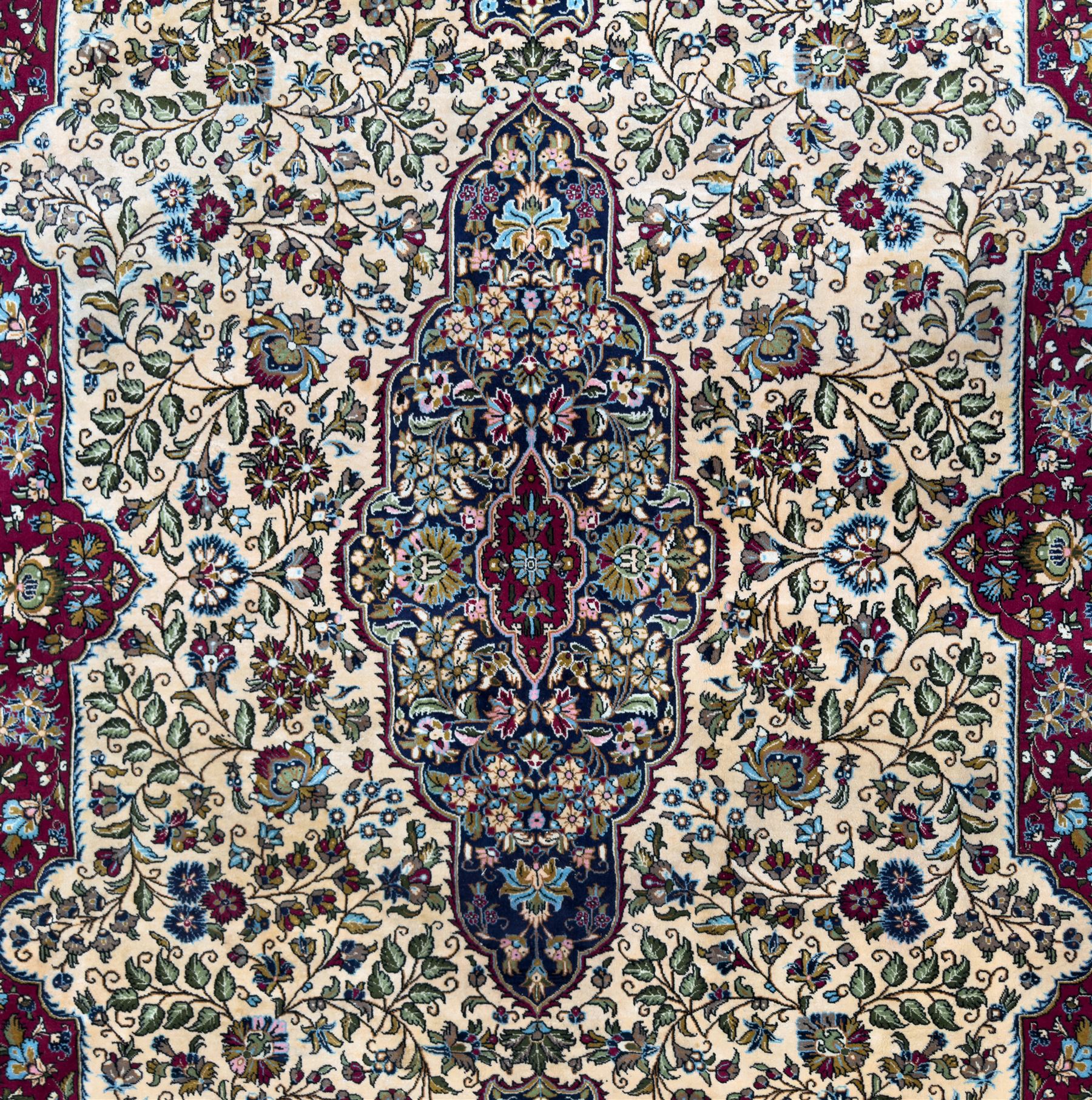 Central Persian Ghom hand-knotted rug, ivory field with scrolling vines, palmettes and flowerheads around a central lobbed medallion with pendants, framed by burgundy spandrels and a navy border of rosettes and arabesques, 289cm x 214cm