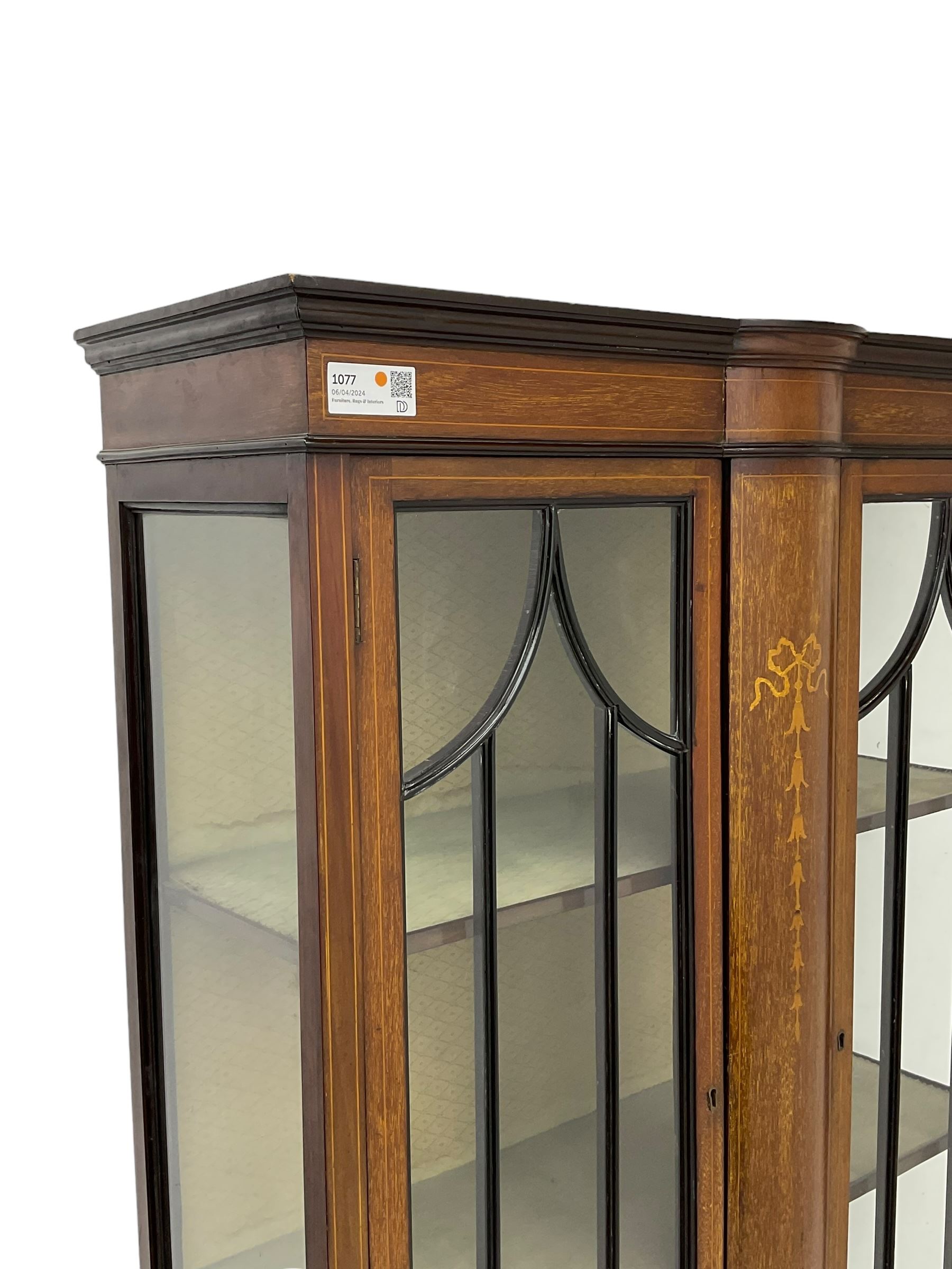 Edwardian inlaid mahogany display cabinet, enclosed by two astragal glazed doors, bowed centre inlaid with ribbon and trailing bellflowers, on square tapering supports with spade feet united by undertier 
