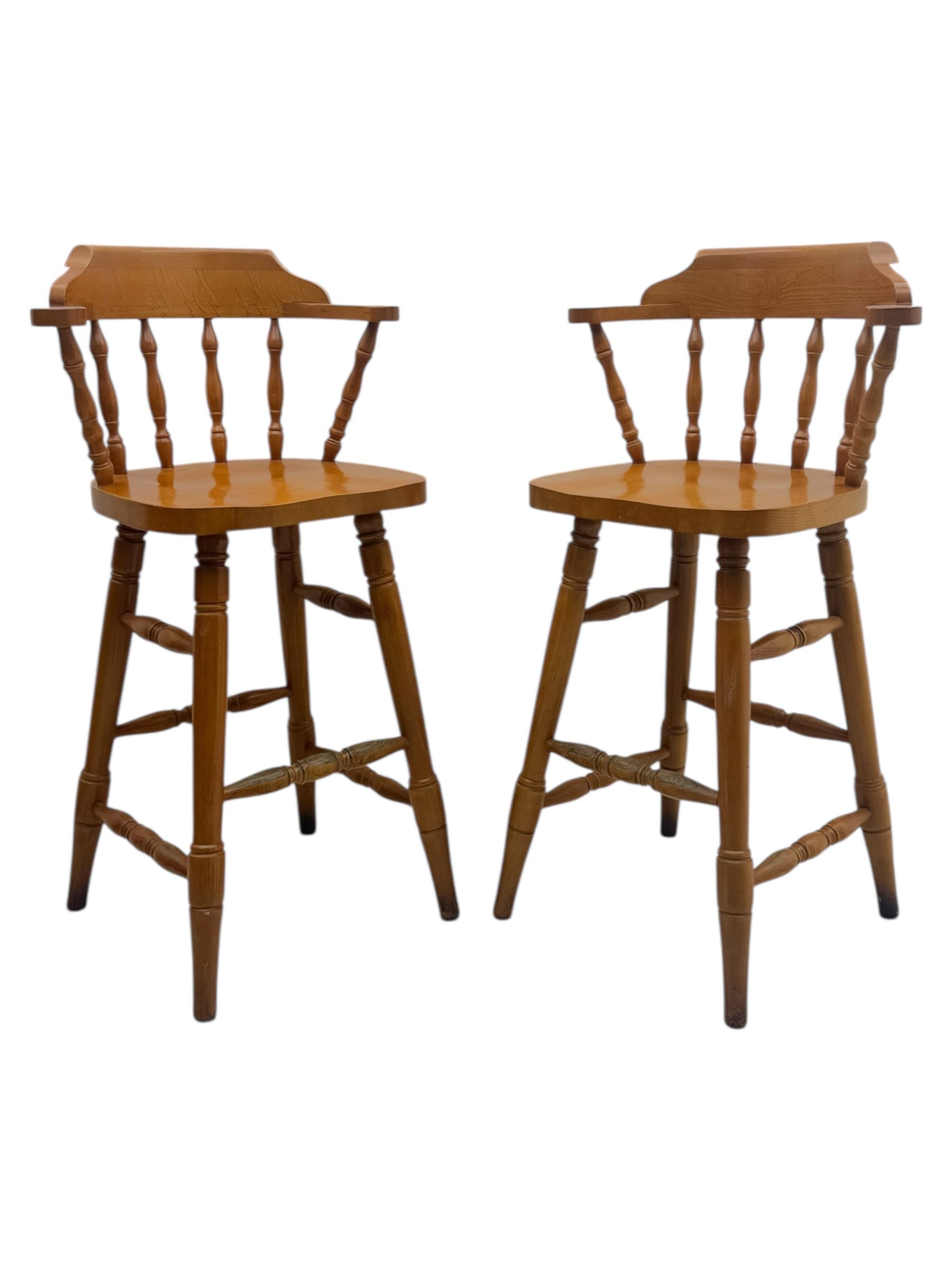 Pair of late 20th century beech bar stools, with curved top rail and turned spindle back, shaped seat over four turned legs united by multiple stretchers