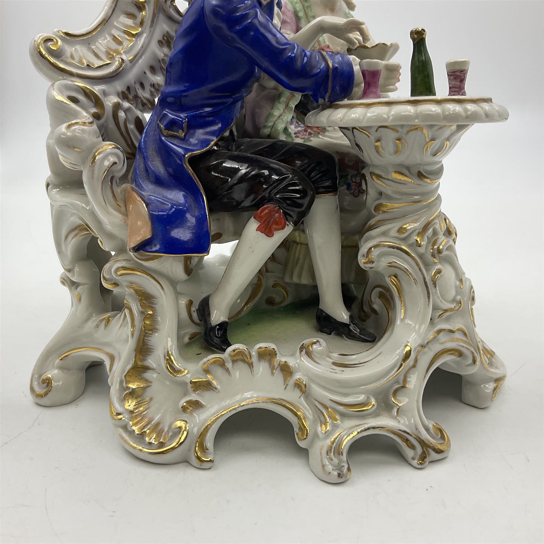 Figure group, probably Volkstedt, modelled as a courting couple seated before a table, the ornate bench and table conforming with and leading from the gilt heightened scrolling base, with blue painted mark beneath, H14.5cm
