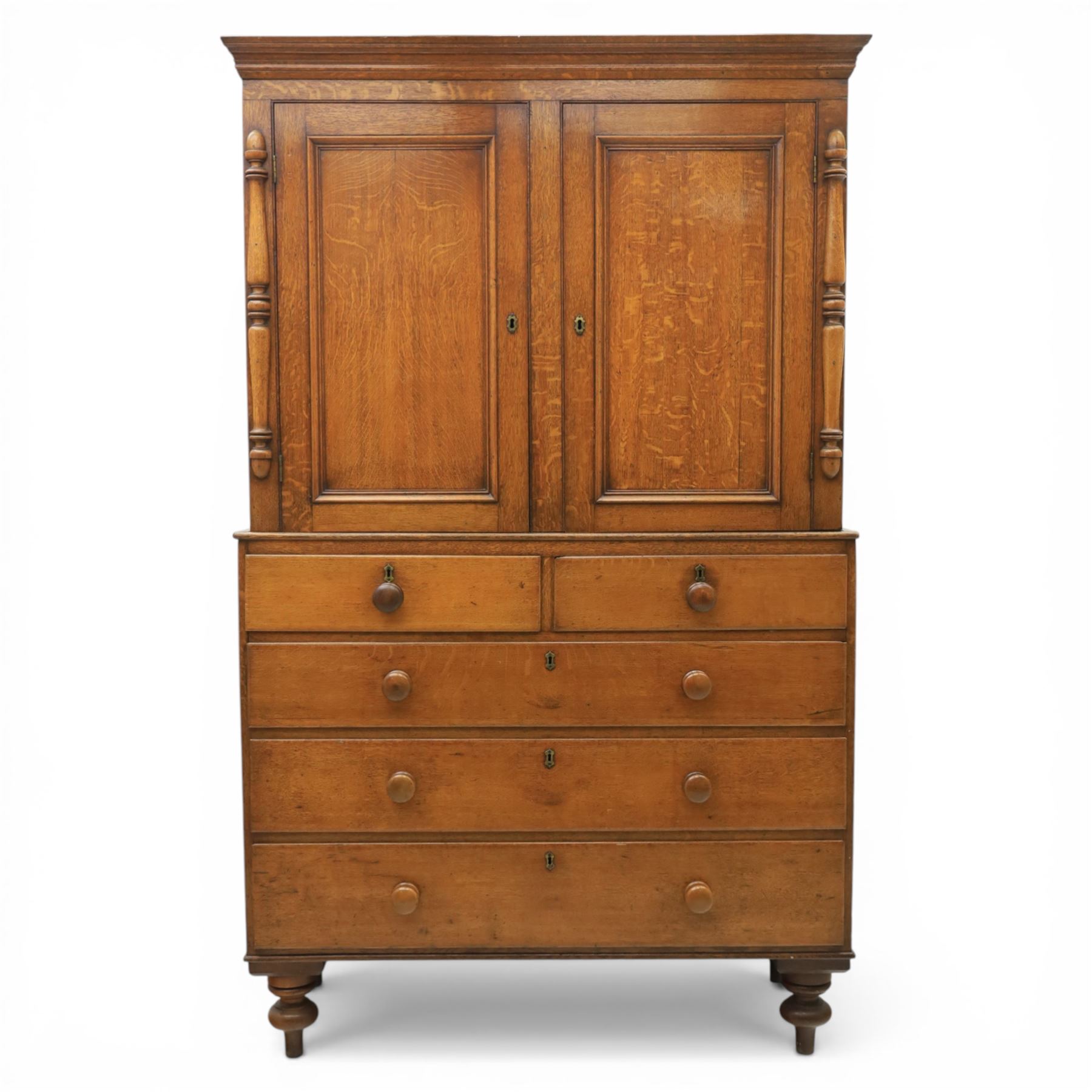 Late 19th century country oak cupboard on chest, cornice top above twin recessed panel doors with central escutcheons, flanked by turned pilasters, the lower chest with two short and three long drawers fitted with turned knob handles, on turned feet