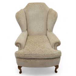 Late 20th century wingback armchair and matching footstool, upholstered in beige embossed fabric with brass stud edging, on cabriole legs and splayed rear legs, together with a matching footstool on turned supports terminating in brass castors (Stool H 42cm, W 75cm, D 47cm)