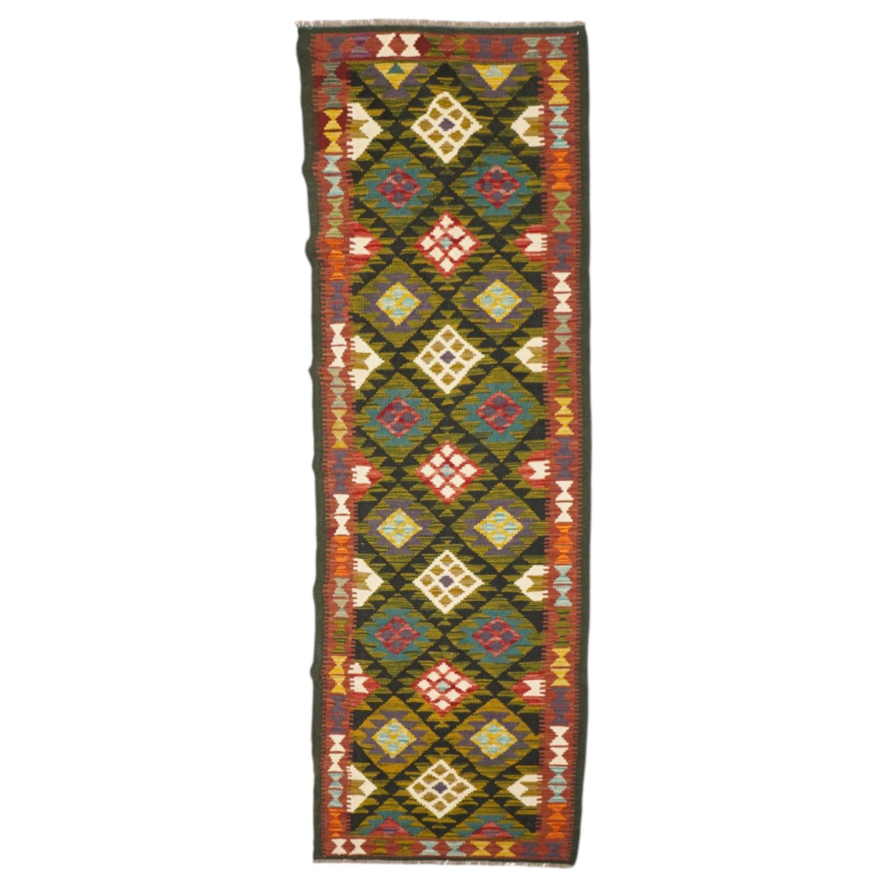 Afghan Maimana flatweave kilim runner, central field features large bold nested diamond motifs and stylized geometric lozenge patterns on olive purple, blue, and green tone ground, border stripe in green ground, and fringe