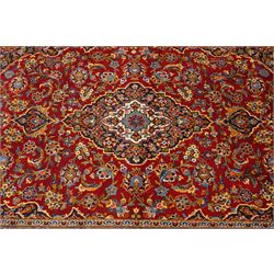 Central Persian Kashan hand-knotted carpet, crimson field with central cusped medallion in ivory, pale blue and indigo, issuing a network of scrolling arabesques, palmettes, and floral sprays, with conforming spandrels, main border of scrolling vinery and stylized palmettes, framed by multiple guard borders, with cotton fringe ends 