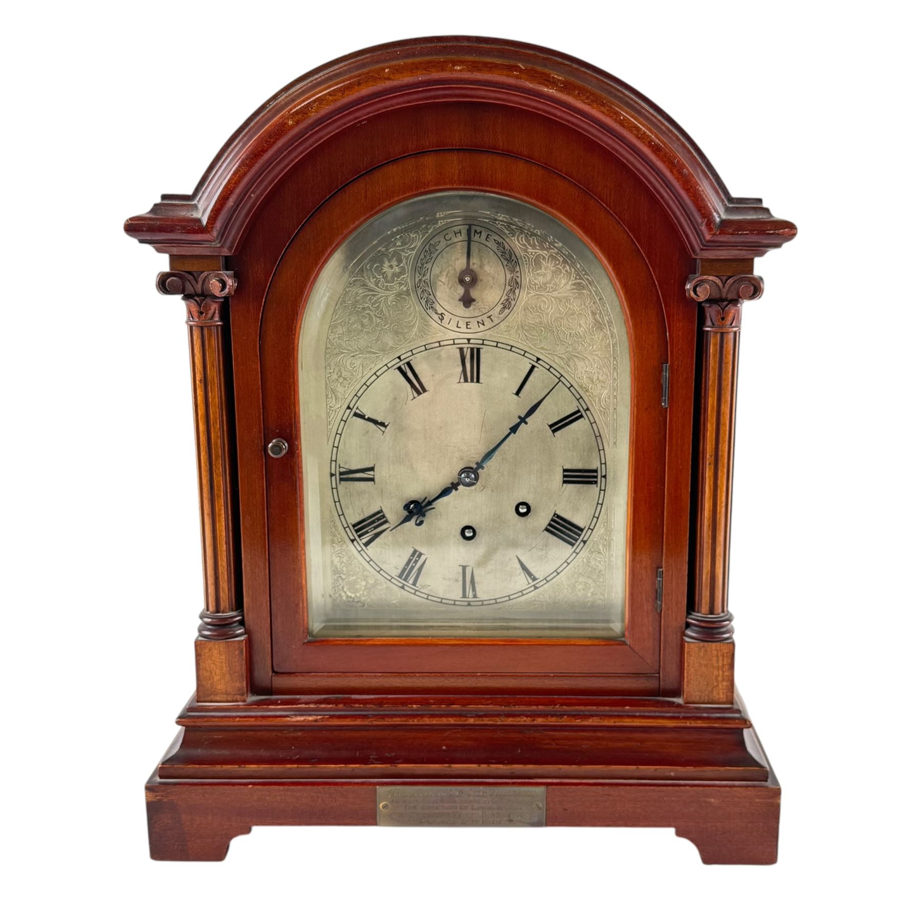 Gustav Becker, German 20th century 8-day mahogany cased mantle clock, break arch mahogany case with a round topped door flanked by reeded pilaster with Ionic capitals and raised on a stepped plinth, the dial with engraved Roman numerals, with steel fleur di Lis hands, and  chime /silent dial, H43cm