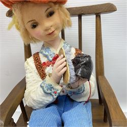 Anna Meszaros Hungary - three hand made needlework figurines - 'The Cobbler' as a child seated in a wooden rocking chair working on a removed boot H24cm; young girl standing crying holding a doll with broken head H32cm; and young girl in long dress and bonnet standing holding a doll H27cm (3)  Auctioneer's Note: Anna Meszaros came to England from her native Hungary in 1959 to marry an English businessman she met while demonstrating her art at the 1958 Brussels Exhibition. Shortly before she left for England she was awarded the title of Folk Artist Master by the Hungarian Government. Anna was a gifted painter of mainly portraits and sculptress before starting to make her figurines which are completely hand made and unique, each with a character and expression of its own. The hands, feet and face are sculptured by layering the material and pulling the features into place with needle and thread. She died in Hull in 1998.