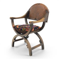 Early 20th century mahogany Savonarola chair, arched leather back with brass studwork, curved open arms with incised geometric decoration, loose patchwork velvet cushion seat, X-frame supports united by circular side rails, on scrolled feet