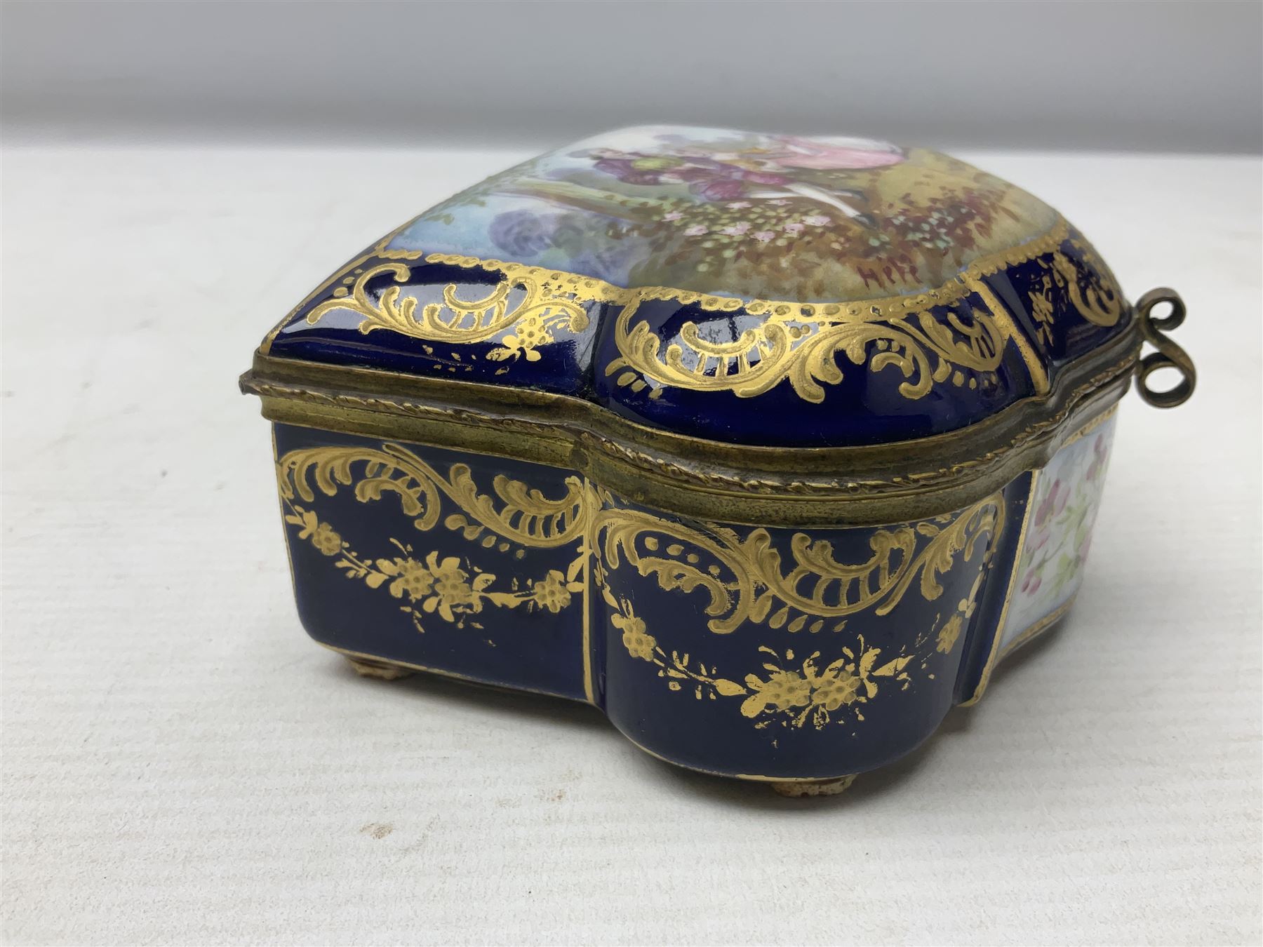 Sevres style late 19th/early 20th century trinket box decorated in the rococo style, the shaped cover painted with an 18th century courting couple in a garden scene opening to reveal the interior painted with floral sprays, the conforming body with a painted panel of floral decoration, all reserved upon cobalt blue ground with foliate gilt borders, with interlaced L's mark beneath, L12cm H6cm