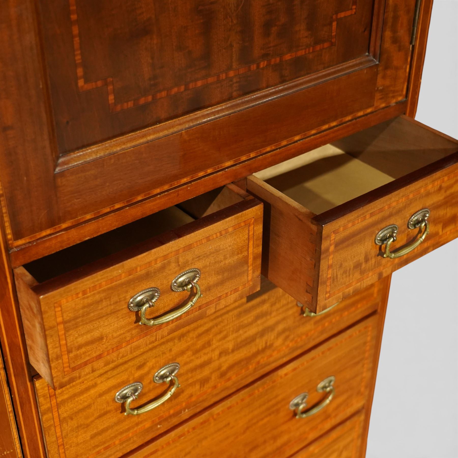 Edwardian mahogany triple combination wardrobe, the moulded cornice above a central panel door inlaid with foliate detail, flanked by full length mirrored doors, the interior fitted with hanging compartments and a central bank of two short and three long drawers, raised on a shaped bracket feet