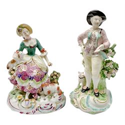 Mid 18th century Derby porcelain figure of a garland shepherd, stood with dog by his feet and letter in his outstretched hand, together with an 18th century porcelain figure, modelled as seated shepherdess with dog upon lap and sheep by her feet, each upon flower encrusted and gilt detailed scrolling base, shepherd with patch marks beneath, shepherd H19cm, shepherdess H15cm