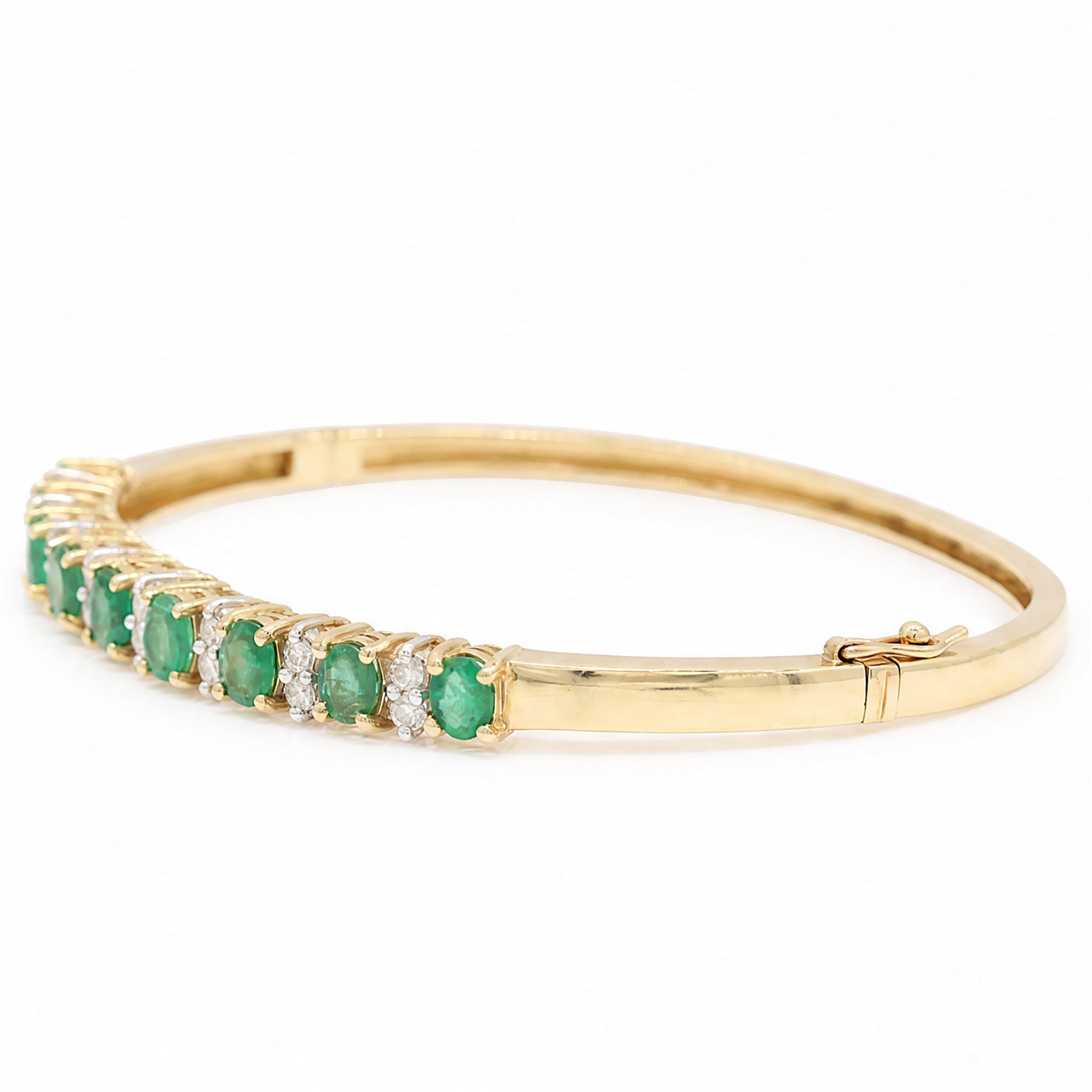 14ct gold emerald and diamond hinged bangle, nine oval cut emeralds, each spaced by two round brilliant cut diamonds, stamped 585, total emerald weight approx  2.15 carat, total diamond weight approx 0.50 carat