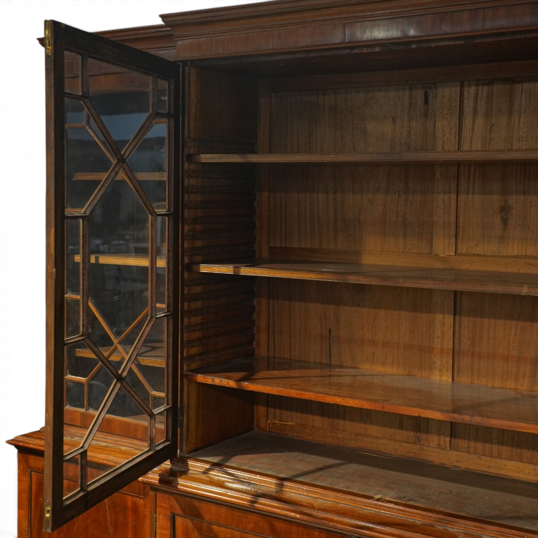 Fine Regency mahogany breakfront library bookcase, the stepped and moulded cornice over four astragal glazed doors enclosing adjustable shelves, the projecting central lower section with a pair of panelled doors enclosing three graduated drawers with brass inset handles above two deep zinc-lined cellarette compartments, flanked by panelled cupboard doors enclosing shelves, the figured mahogany fronts with ebony line inlay, on moulded plinth bases