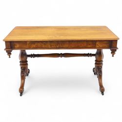 Mid Victorian walnut library table, plain top of rectangular form with moulded edge above frieze fitted with opposing drawers, table supported on a pair of turned and hexagonal carved baluster end standards, united by a turned stretcher terminating in scrolling sabre legs carved with acanthus and floral details, resting on ceramic castors, circa 1860