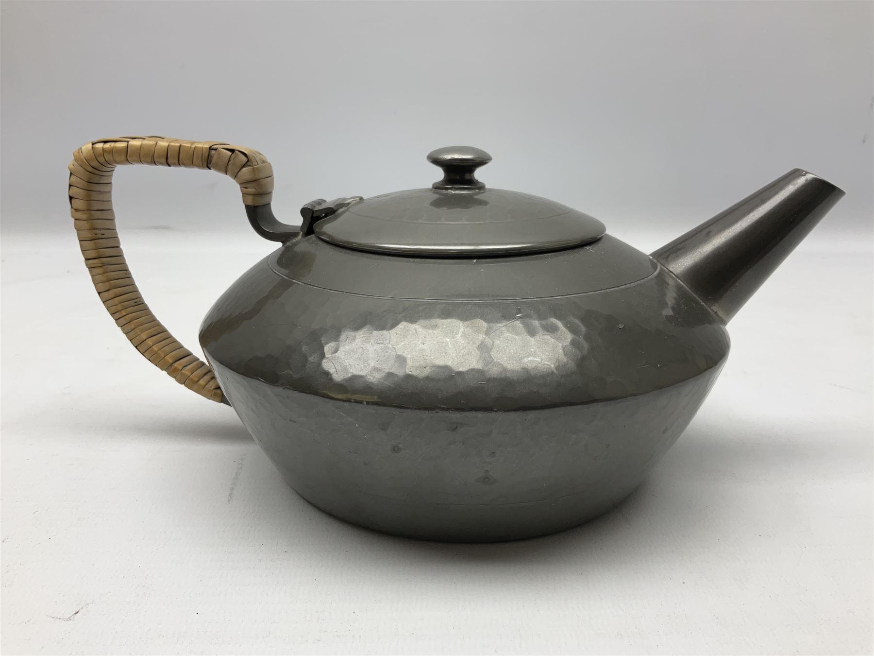 Liberty & Co Tudric pewter three piece tea service, comprising teapot with woven reed handle, twin handled open sucrier, and milk jug, each of squat form with planished finish, each impressed beneath Tudric Pewter Ware 01537 Made in England, together with a matched unmarked tray