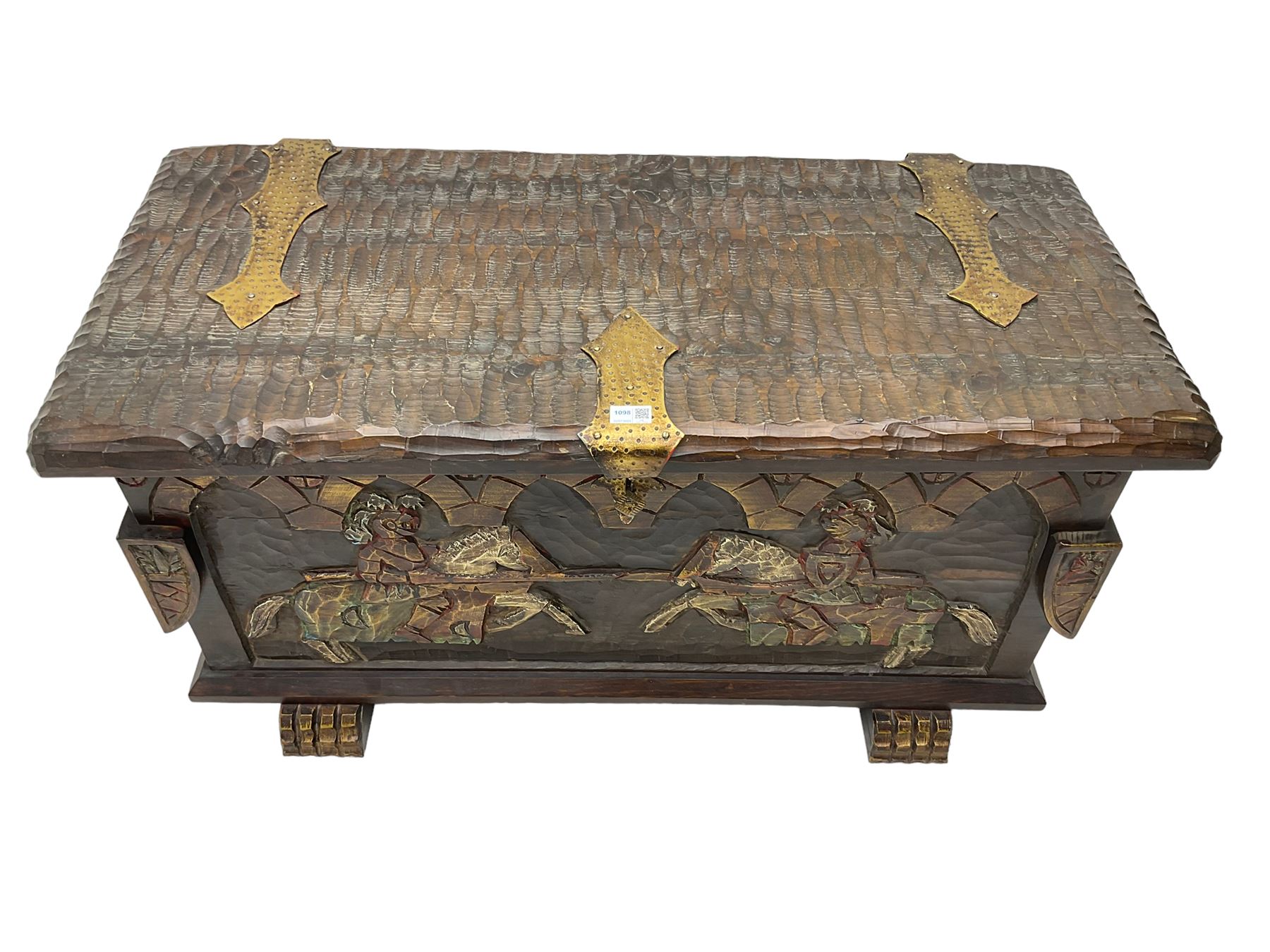 Carved wooden blanket chest, the tooled hinged lid with shaped metal strap hinges and catch, the front carved with arcade over two medieval jousters, on carved sledge feet