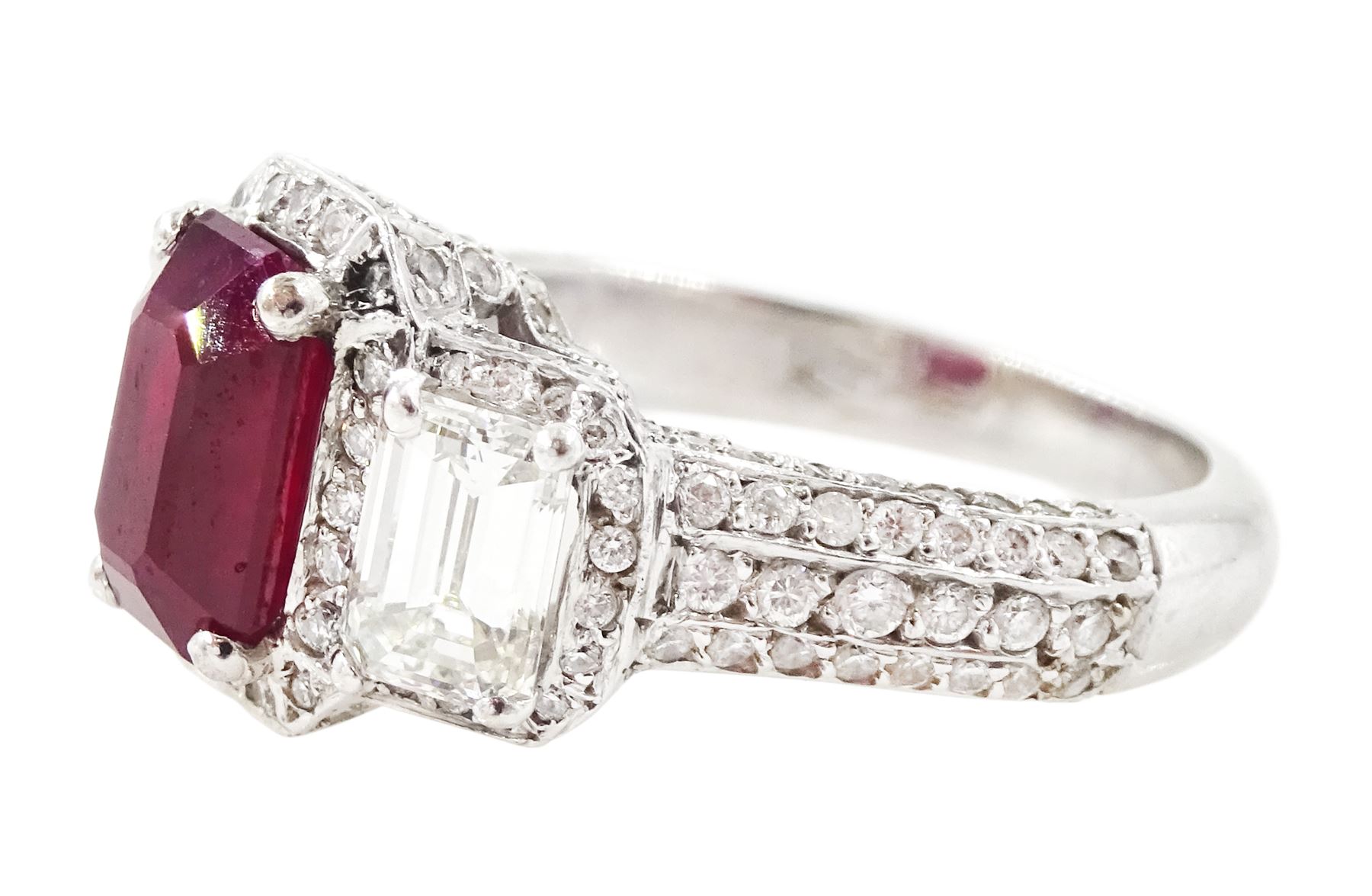 18ct white gold ruby and diamond trilogy ring, single emerald cut ruby of approx 1.85 carat, with a single emerald cut diamond set either side, all surrounded by round brilliant cut diamonds, the shoulders set with three rows of round brilliant cut diamonds, principal two emerald cut diamonds approx 1.10 carat