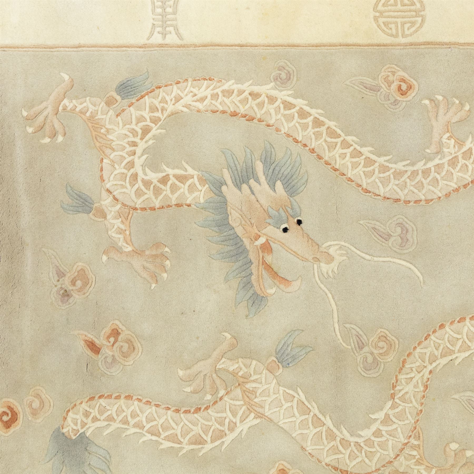 Chinese wool rug, the pale grey central field decorated with two stylised dragons, flaming pearls and cloud scrolls, within a cream border of shou medallions and geometric motifs, with cotton fringe ends