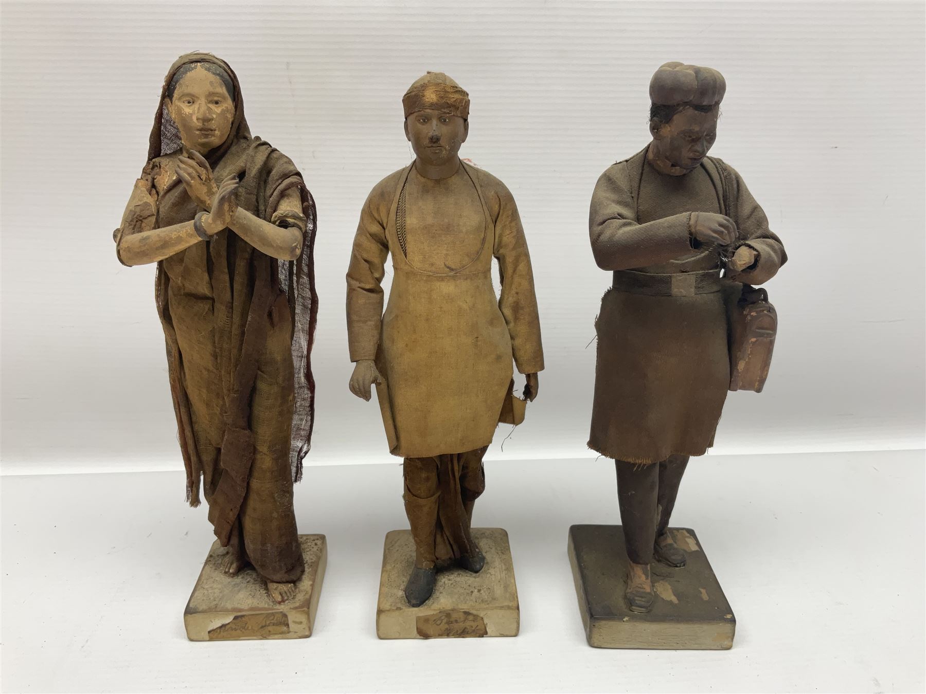 Seven 19th Century Indian clay dolls, possibly Krishnanagar, each figure with painted details, wearing cloth garments, standing on rectangular bases, some with paper label to the base, H25cm