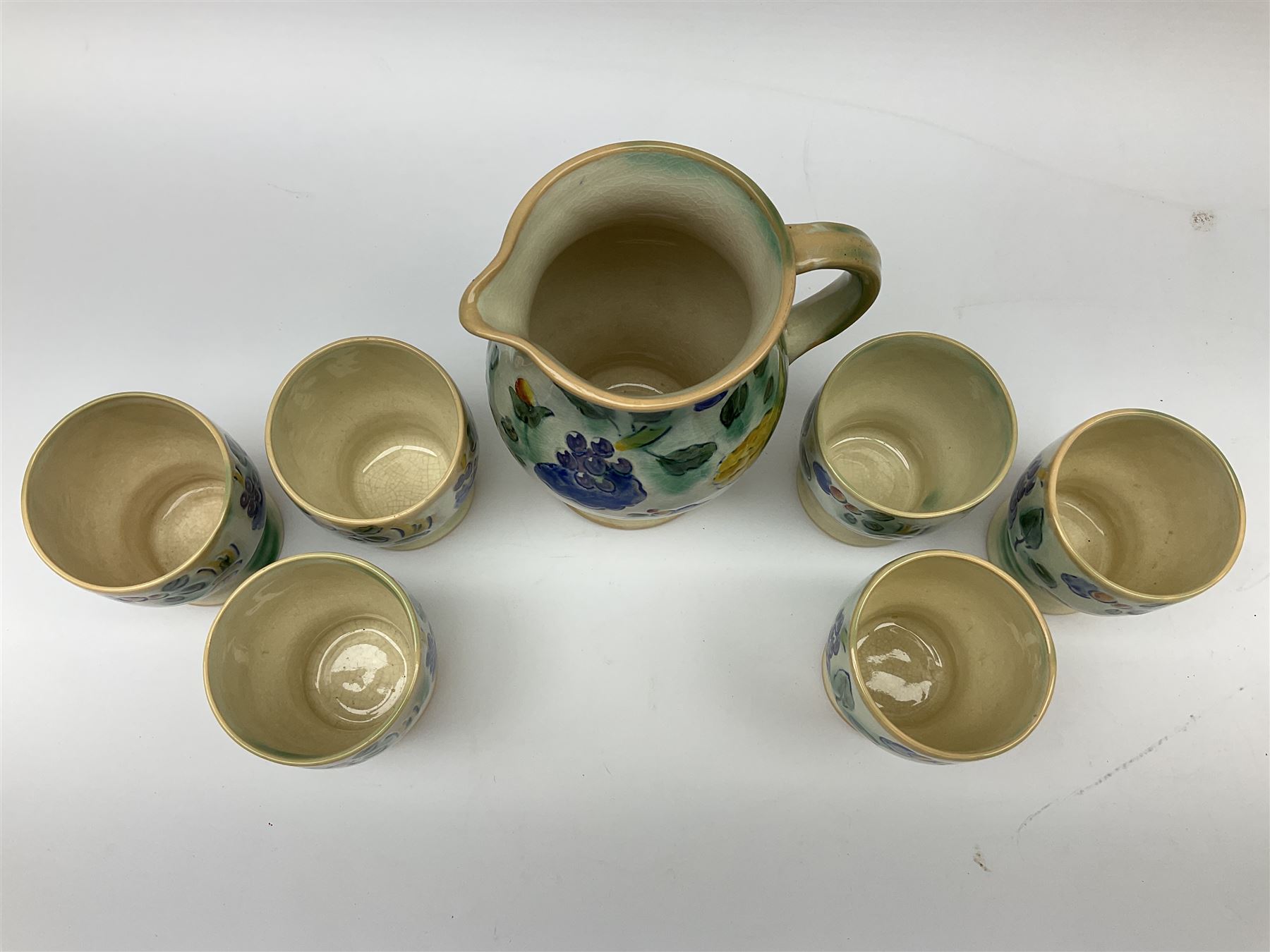Early 20th century Royal Doulton Brangwyn Ware jug and set of six beakers, designed by Frank Brangwyn RA, all decorated in the Harvest pattern with stylised leaves and fruit on mottled peach and green ground, all with printed marks beneath, date code for 1920s, largest H18cm