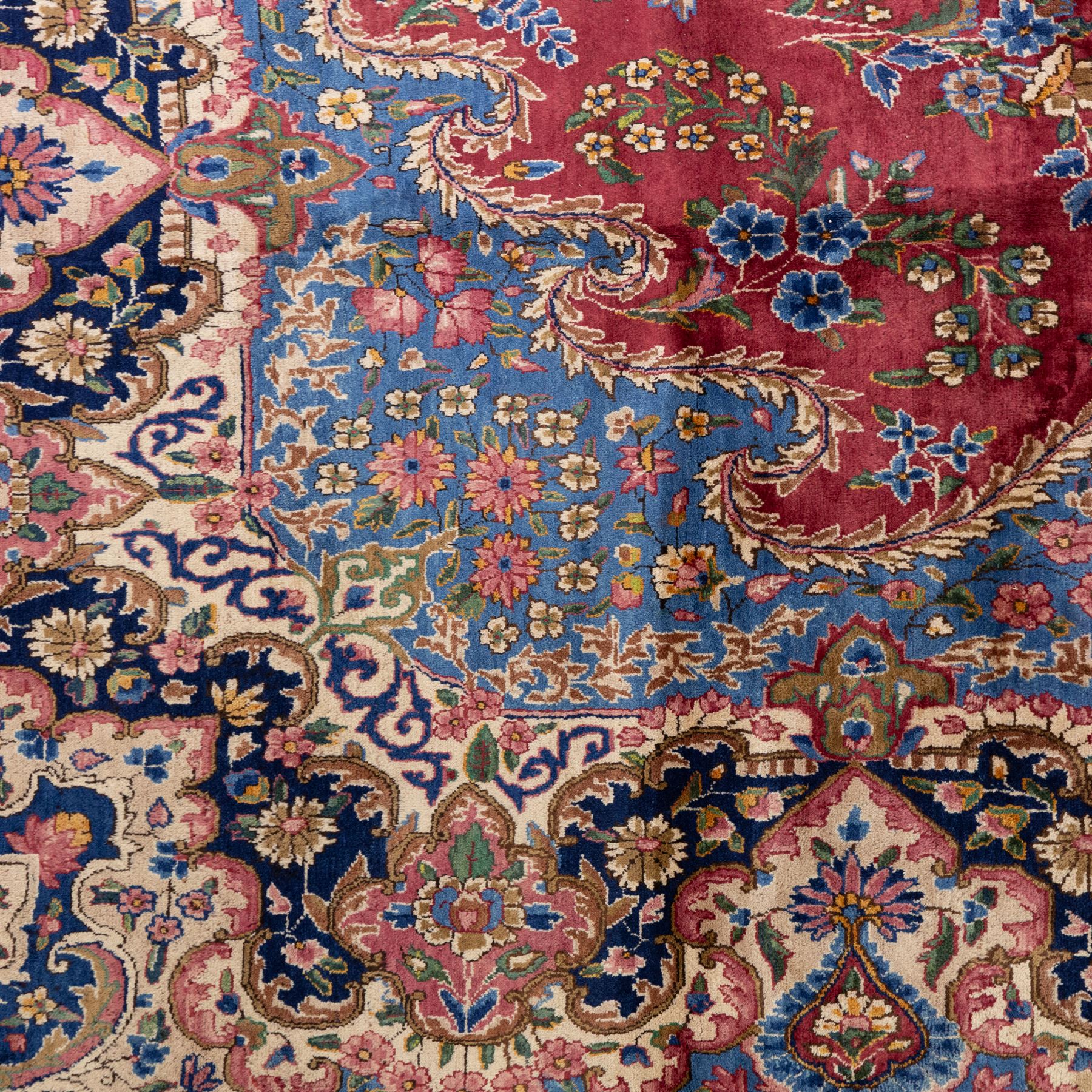 Large Central Persian Kirman hand-knotted carpet, raspberry red field, with central shaped medallion surrounded by an intricate arrangement of scrolling vines and floral sprays, within conforming spandrels and a pale blue border decorated with floral motifs, enclosed by guard stripes, with cotton fringe ends 